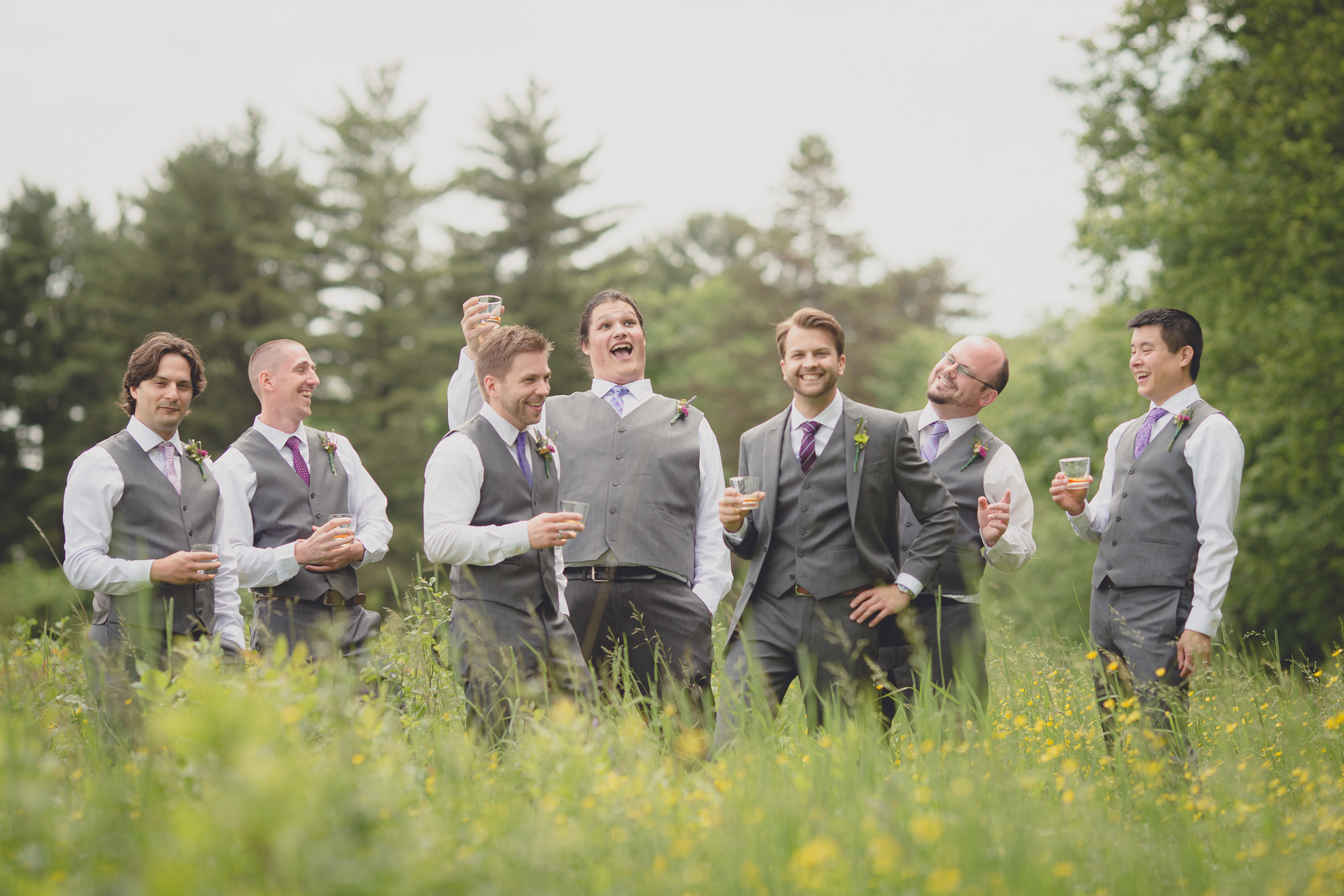 groomsmen pose for portraits in field with whiskey glasses at small wedding at Knox Farm near Buffalo, NY