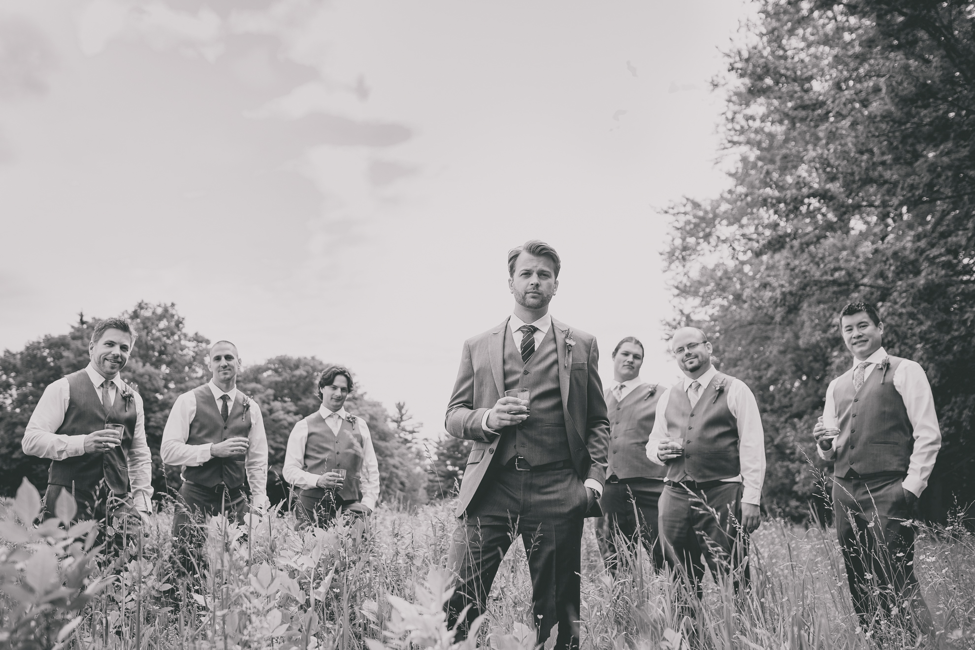 groomsmen pose for portraits in field with whiskey glasses at small wedding at Knox Farm near Buffalo, NY