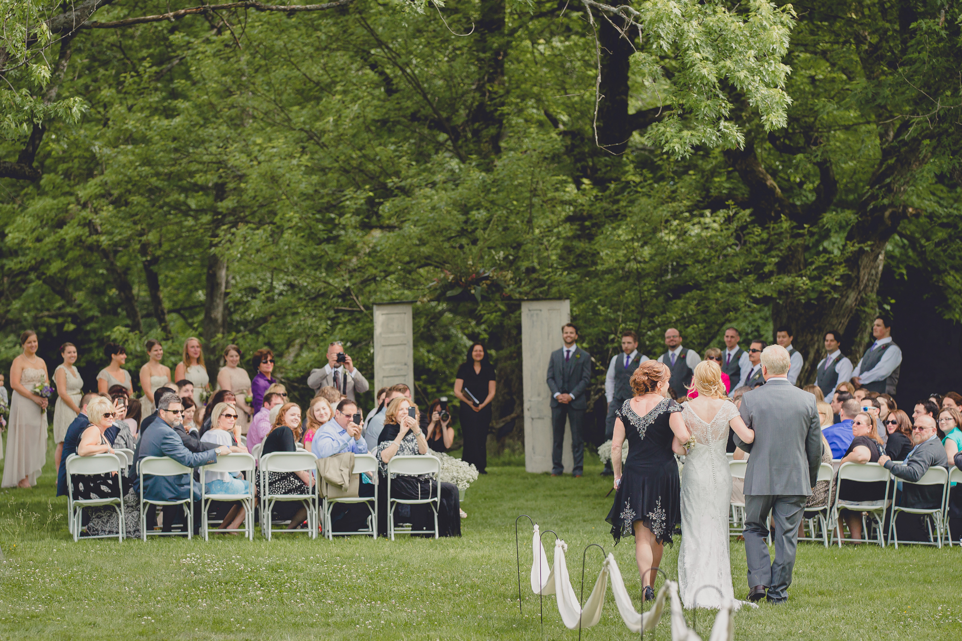 mother and father of bride escort bride through grass before ceremony at wedding at Knox Farm near Buffalo, NY