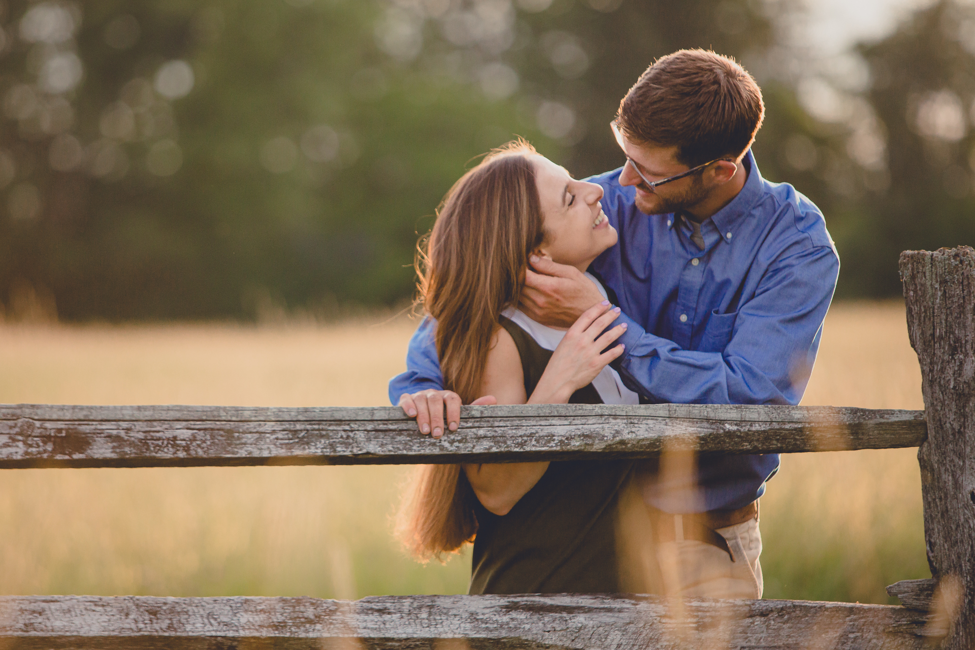 bride and groom kiss in field during wedding engagembride and groom look at each other and embrace along old wood fence during wedding engagement photography at Knox Farm State Park near Buffalo, NYent photography at Knox Farm State Park near Buffalo, NY