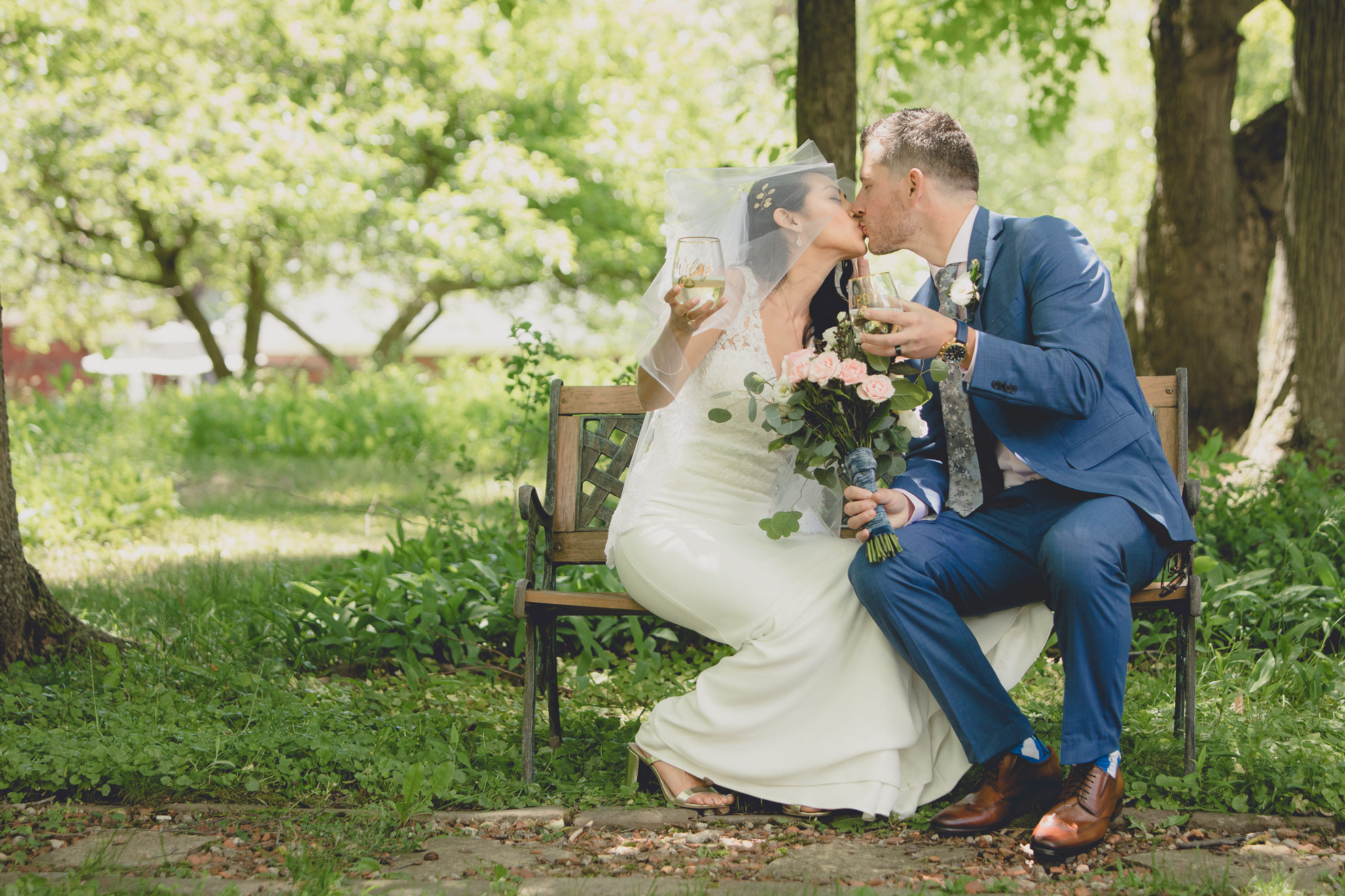 bride and groom kiss on bench in forest after small backyard micro wedding in Buffalo, NY
