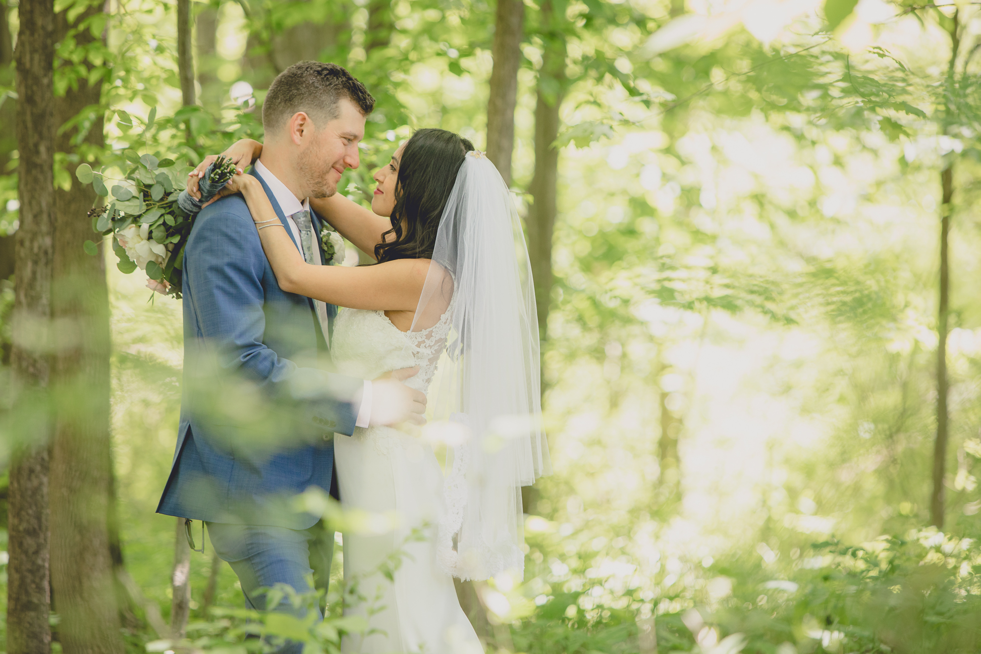 bride and groom look at each other while embracing in woods after small backyard micro wedding in Buffalo, NY