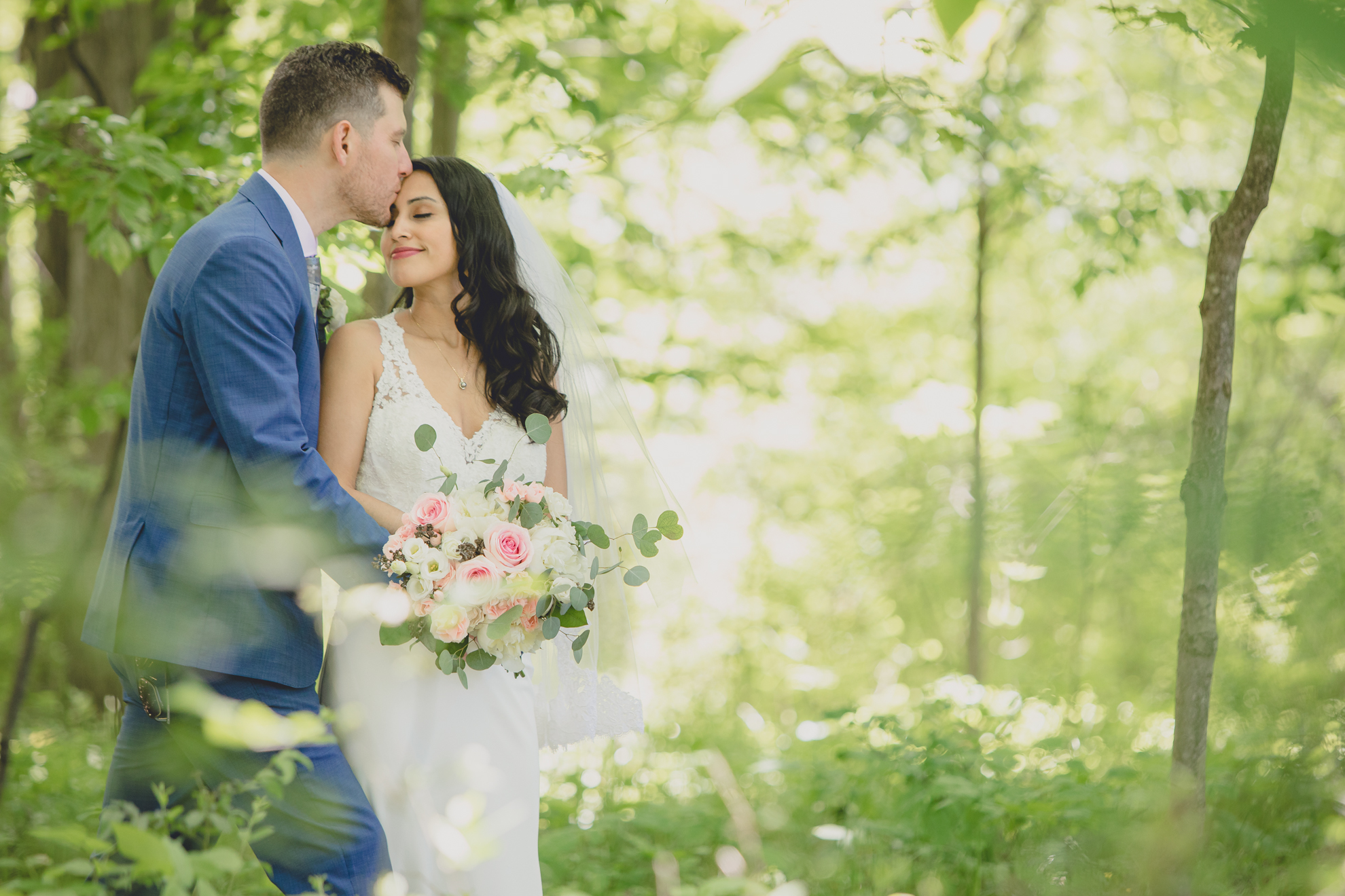 groom kisses bride's forehead in forest after small backyard micro wedding in Buffalo, NY