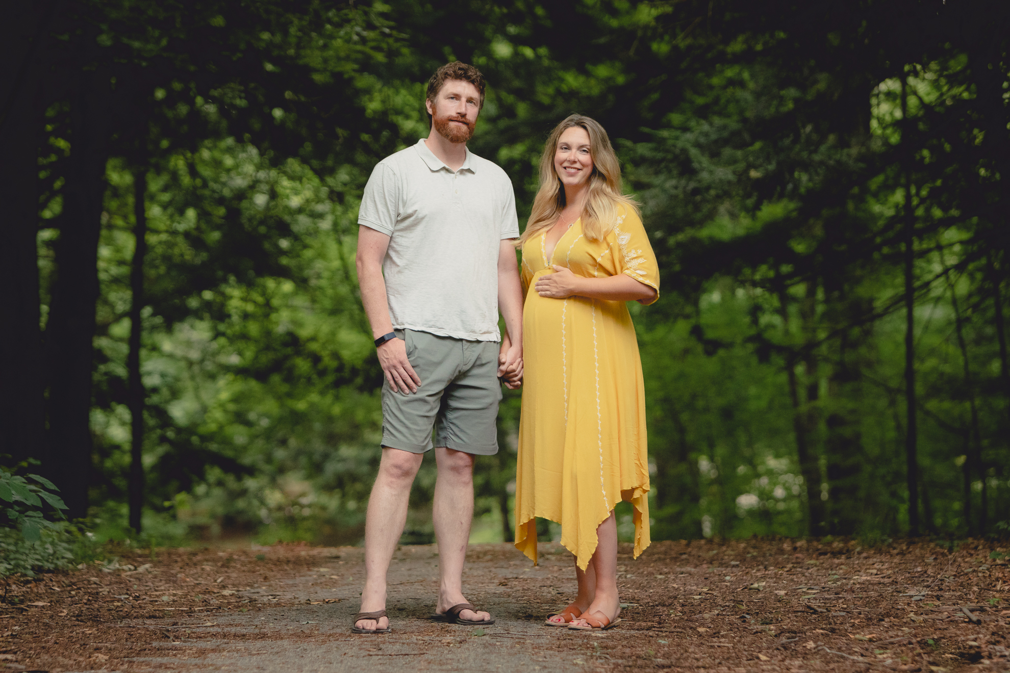 maternity portrait of pregnant mother with husband holding hands and smiling for photographer in forest at Chestnut Ridge Park near Buffalo, NY