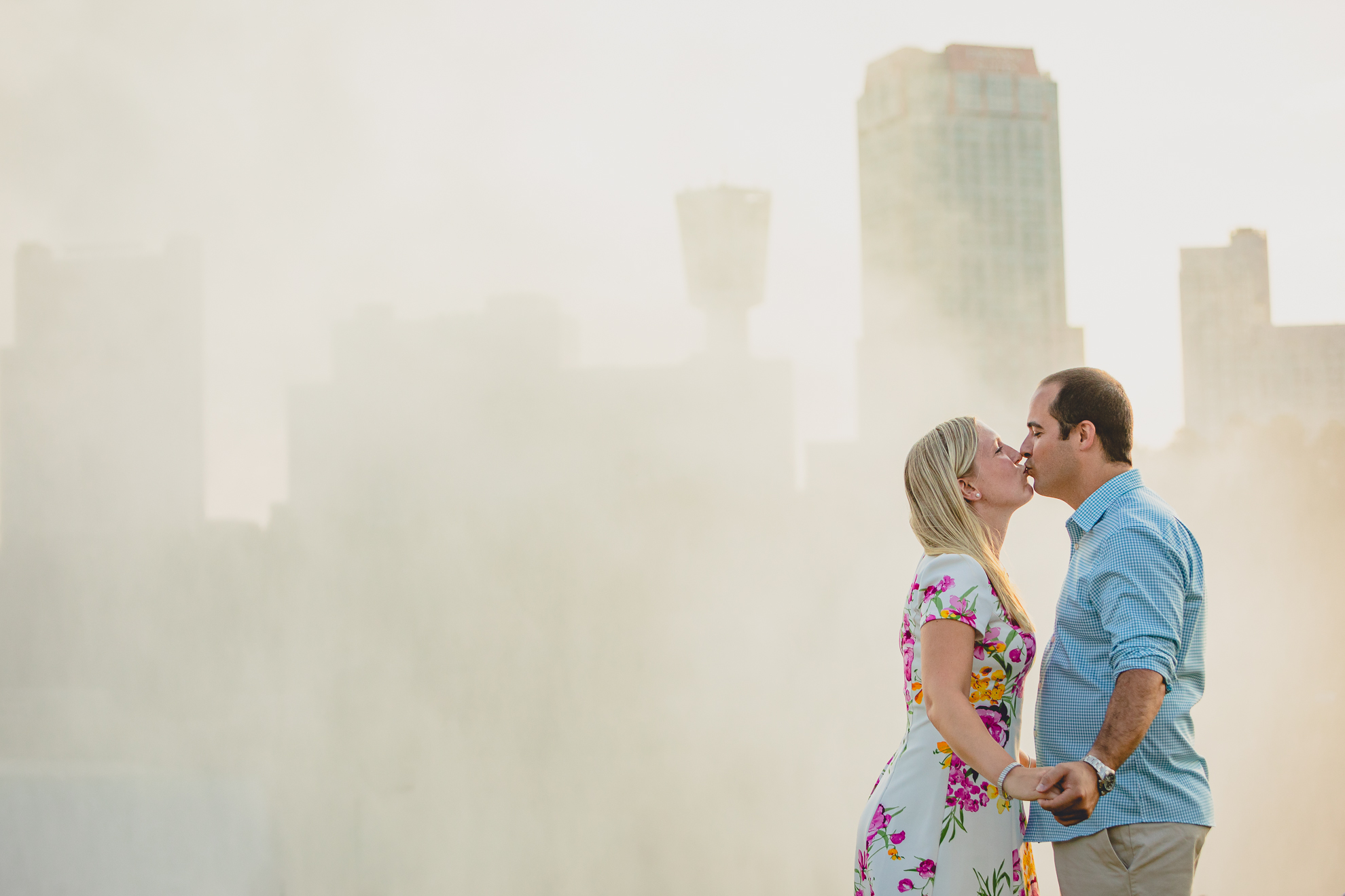 engaged couple kisses with Niagara Falls mist and skyline in the background during their wedding engagement photography session 
