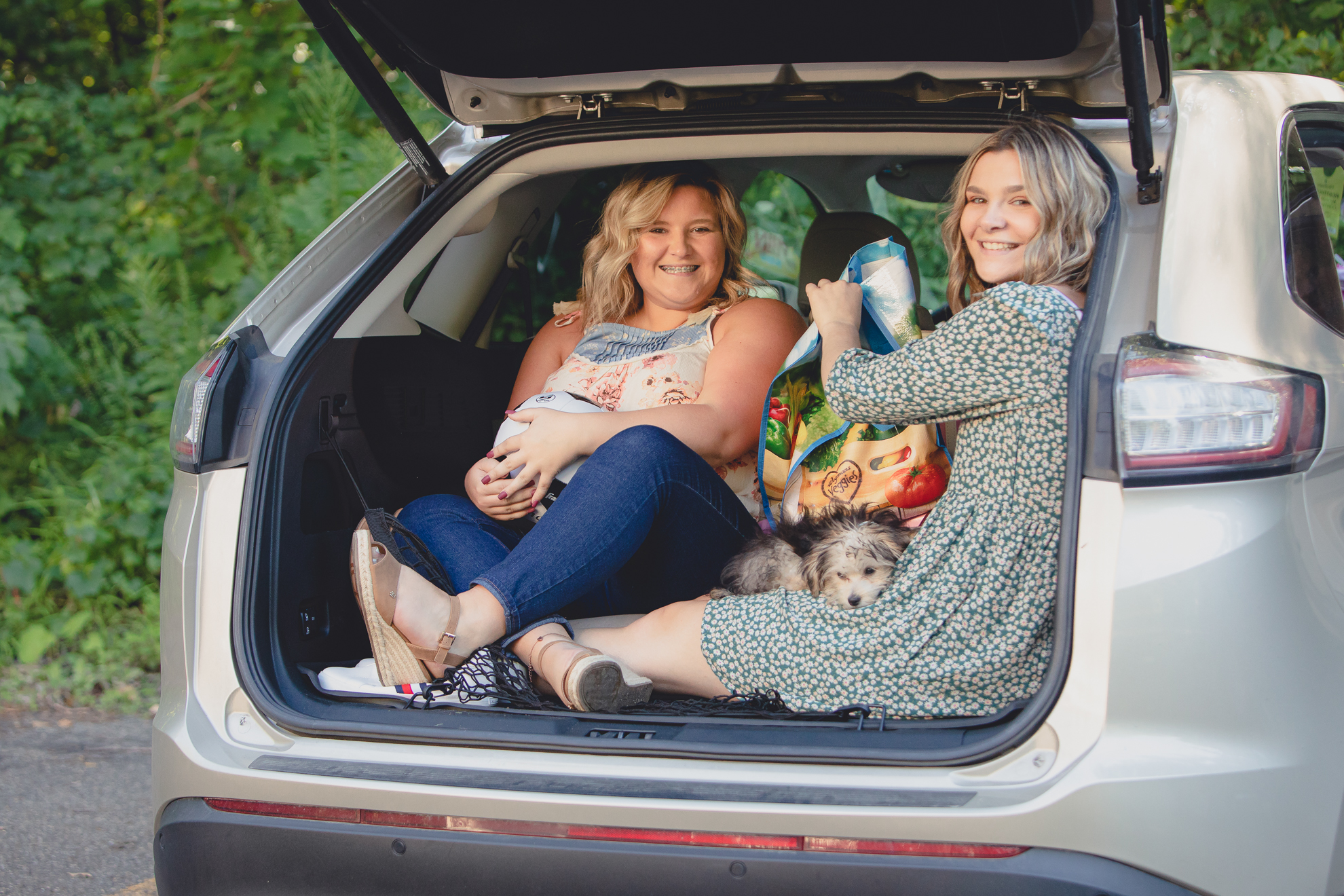 maple grove high school student smiles poses for photographer with sister in back of car during senior portrait photography session at Chautauqua Institution