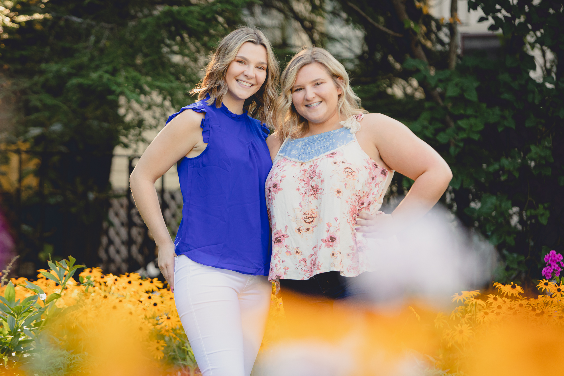 maple grove high school student smiles poses for photographer in garden with sister during senior pictures at Chautauqua Institution