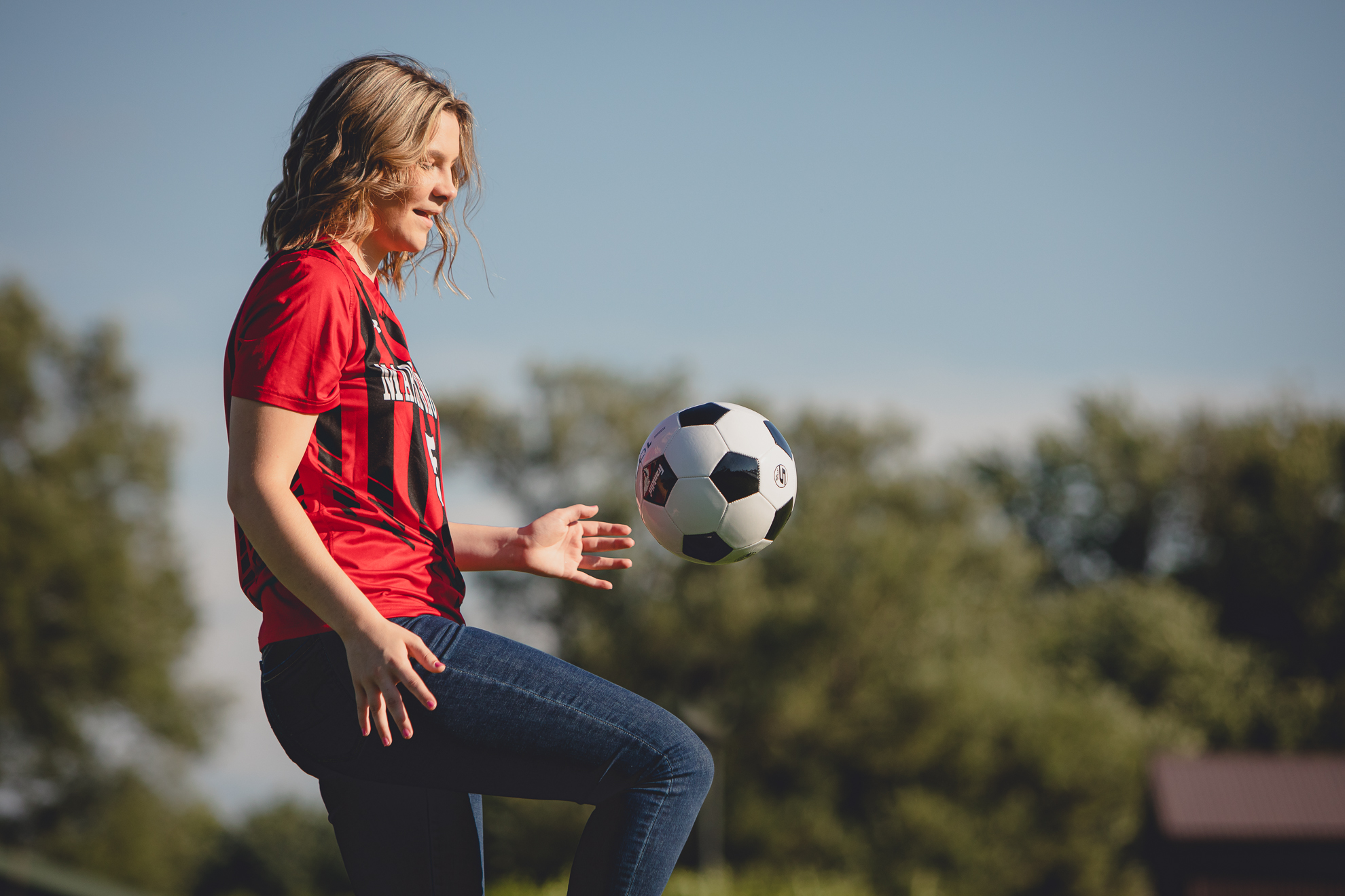 maple grove high school student smiles poses for photographer while wearing jersey in soccer field during senior pictures at Chautauqua Institution