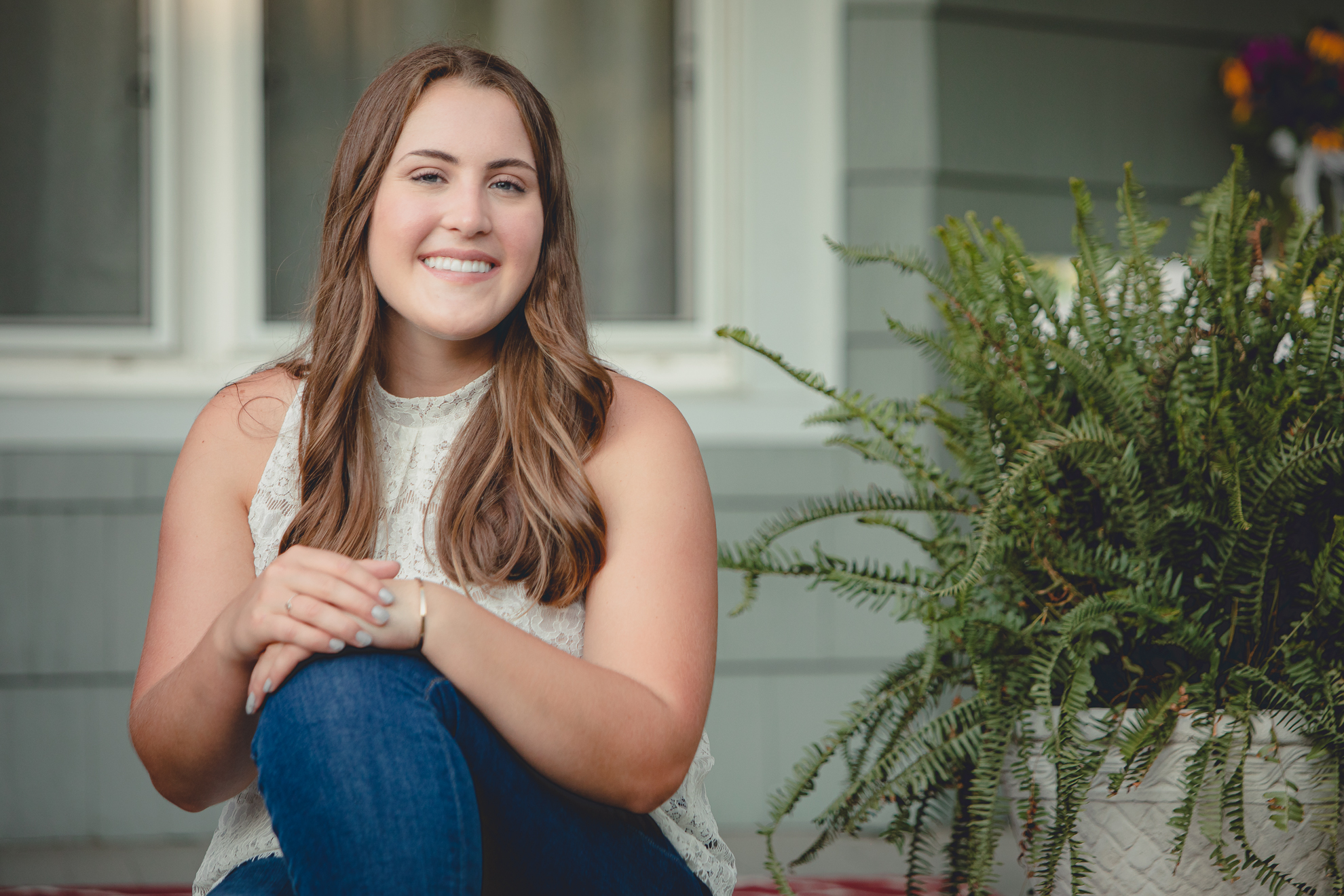 Tessa smiles for photographer on front porch steps during her senior portrait photography session in WNY
