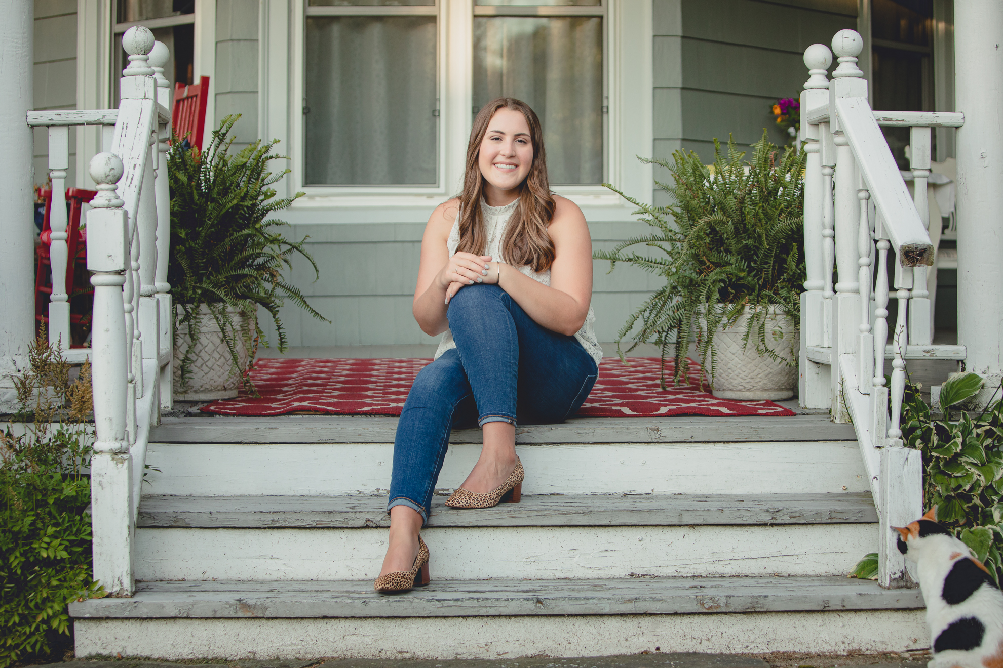 Tessa smiles for photographer on front porch steps while cat looks on during her senior portrait photography session in WNY