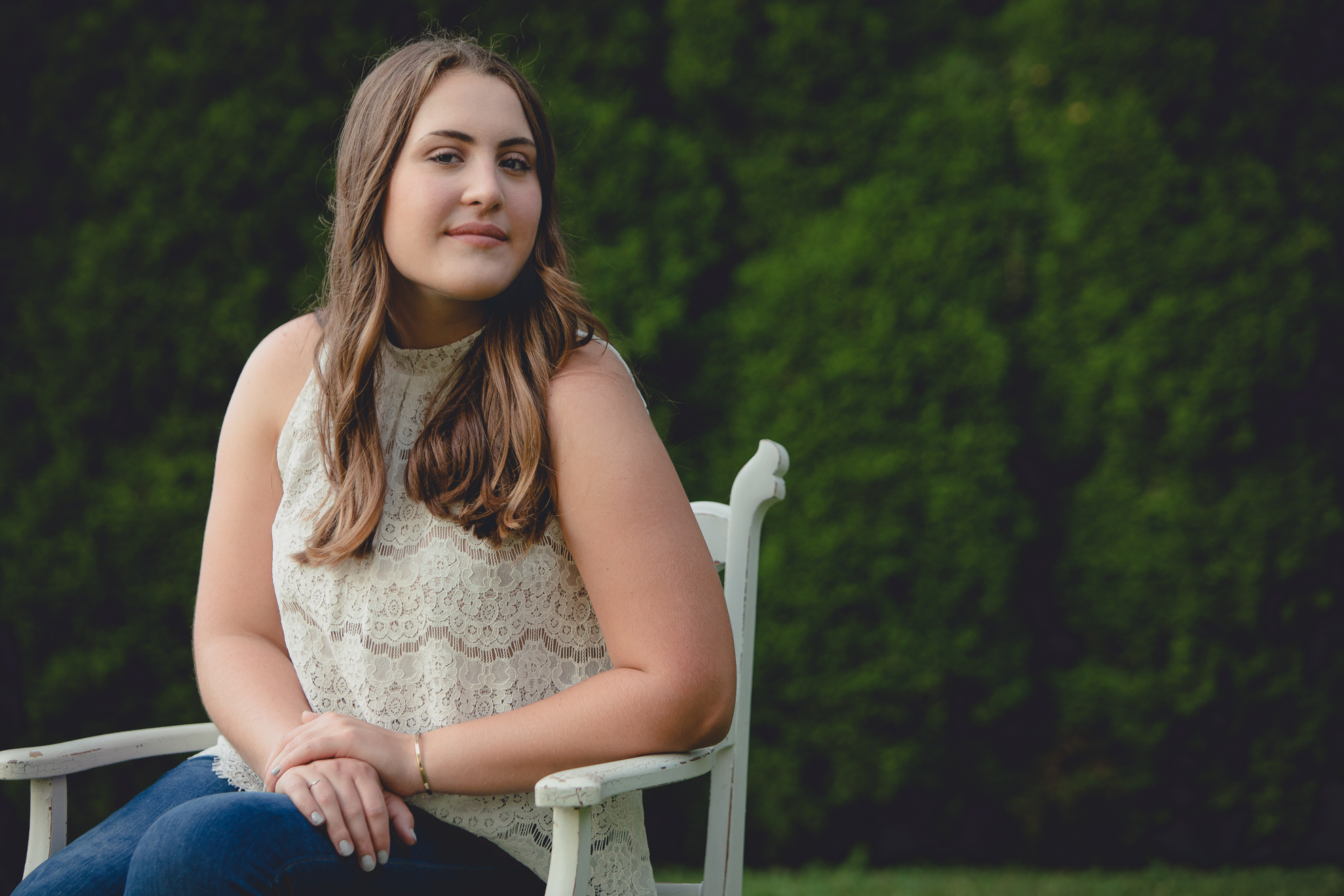 Tessa sits on vintage chair in yard during senior portrait photography session near Buffalo, NY