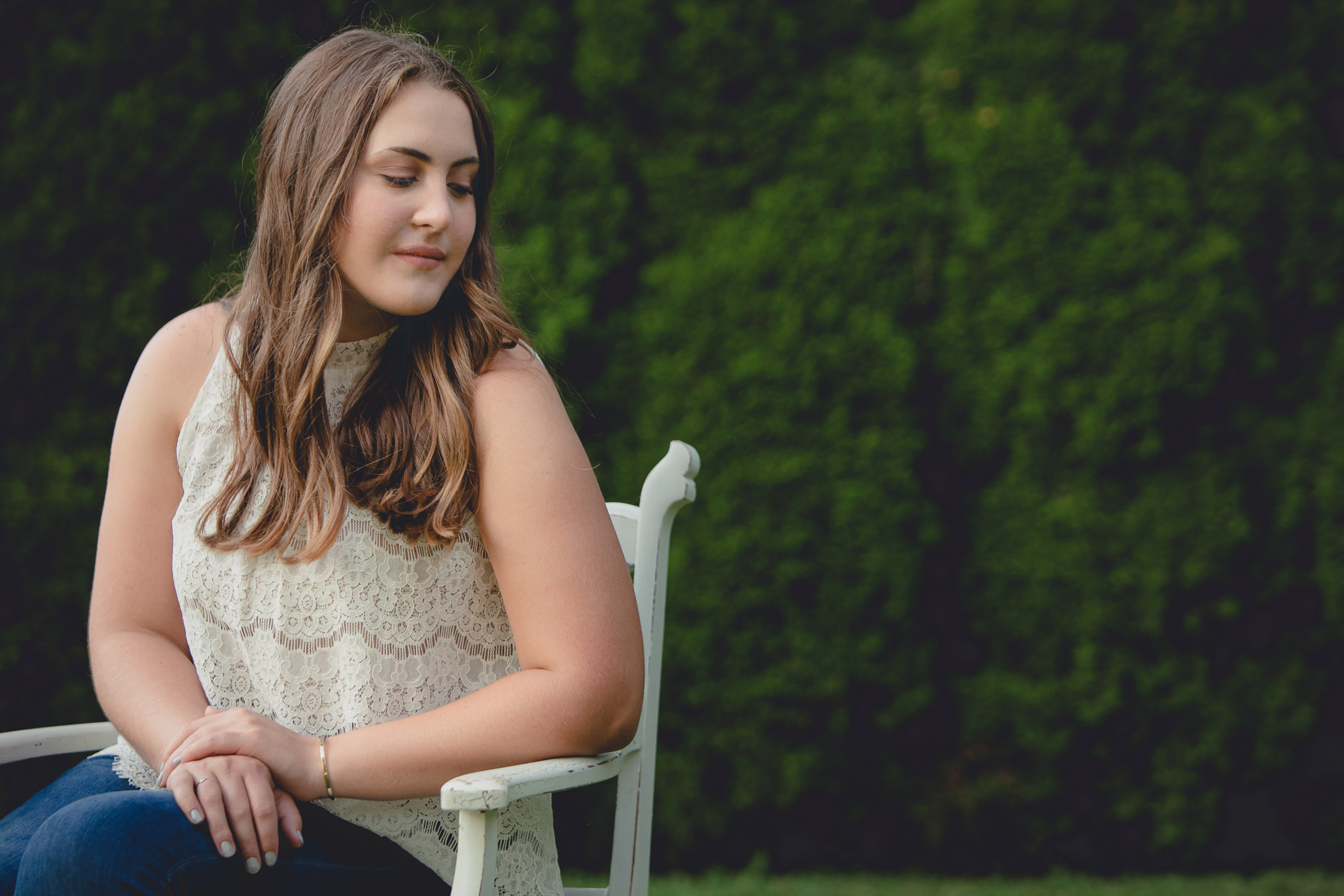 Tessa sits on vintage chair in yard during senior portrait photography session near Buffalo, NY