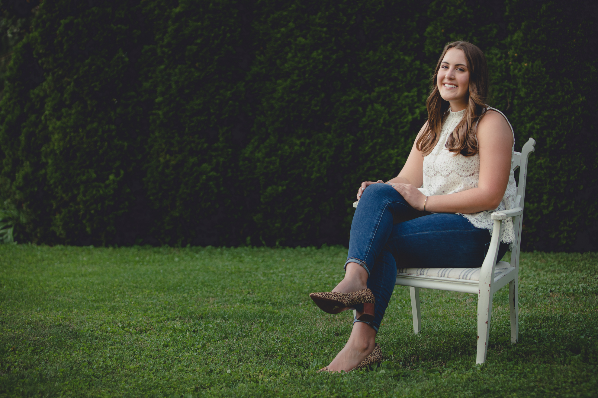 Tessa sits on vintage chair in yard during senior portrait photography session near Buffalo, NY