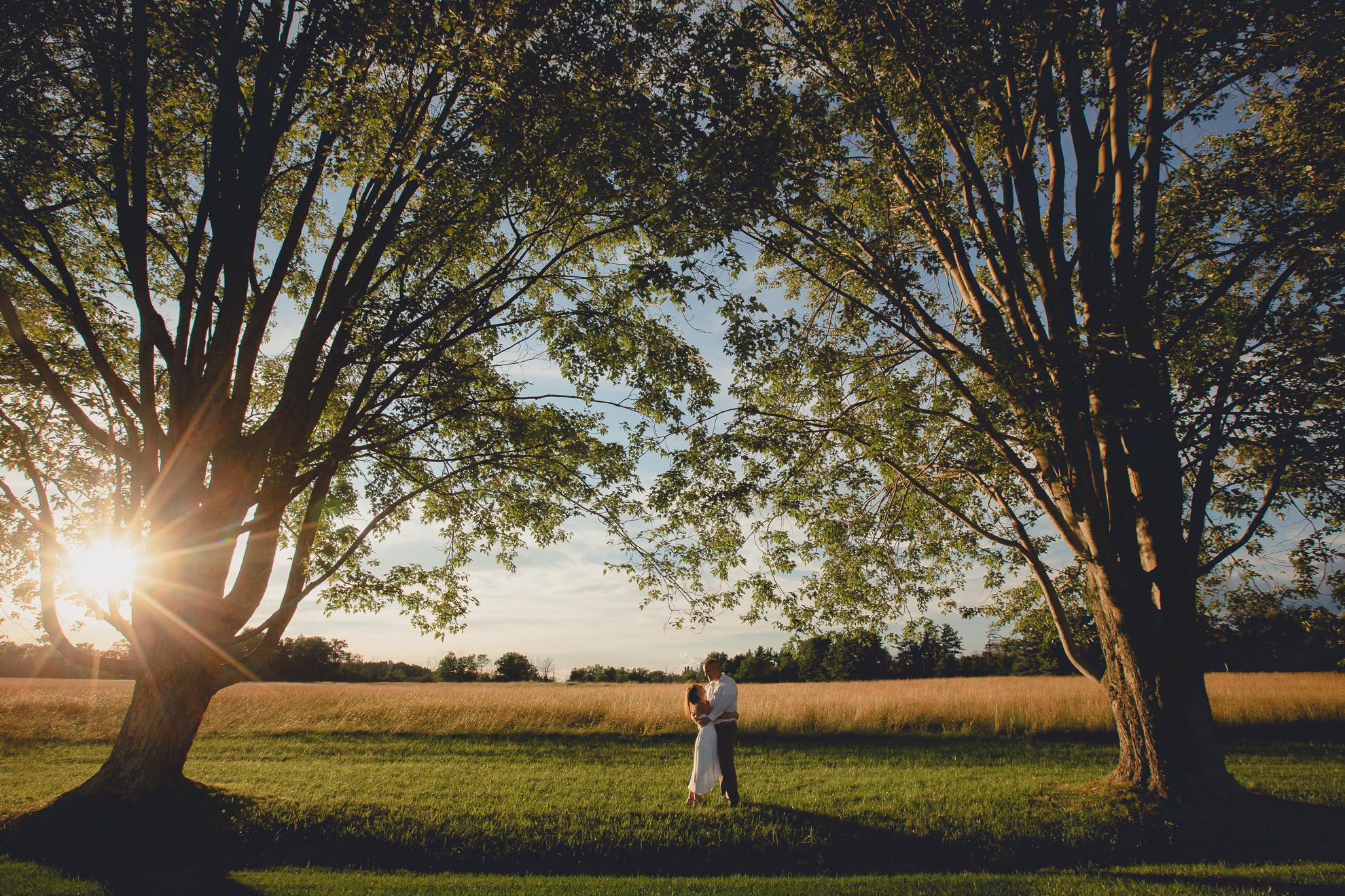 bride and groom slow dance between two trees at sunset groom wraps arms around bride in field during wedding photography engagement portrait session at Knox Farm near Buffalo, NY