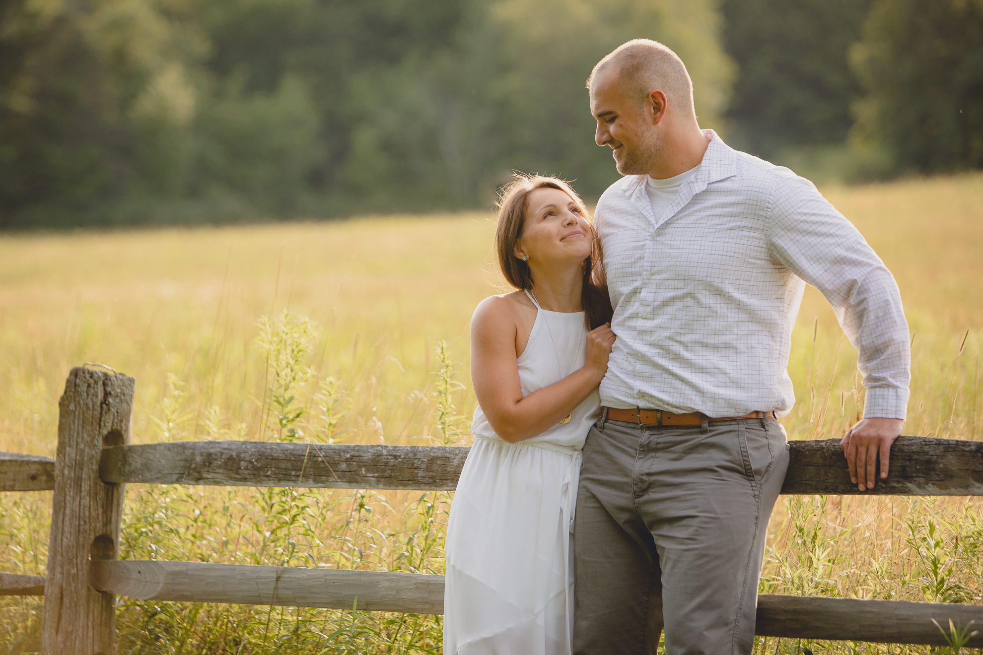 couple looks at each other against old fence in field during wedding photography engagement portrait session at Knox Farm near Buffalo, NY