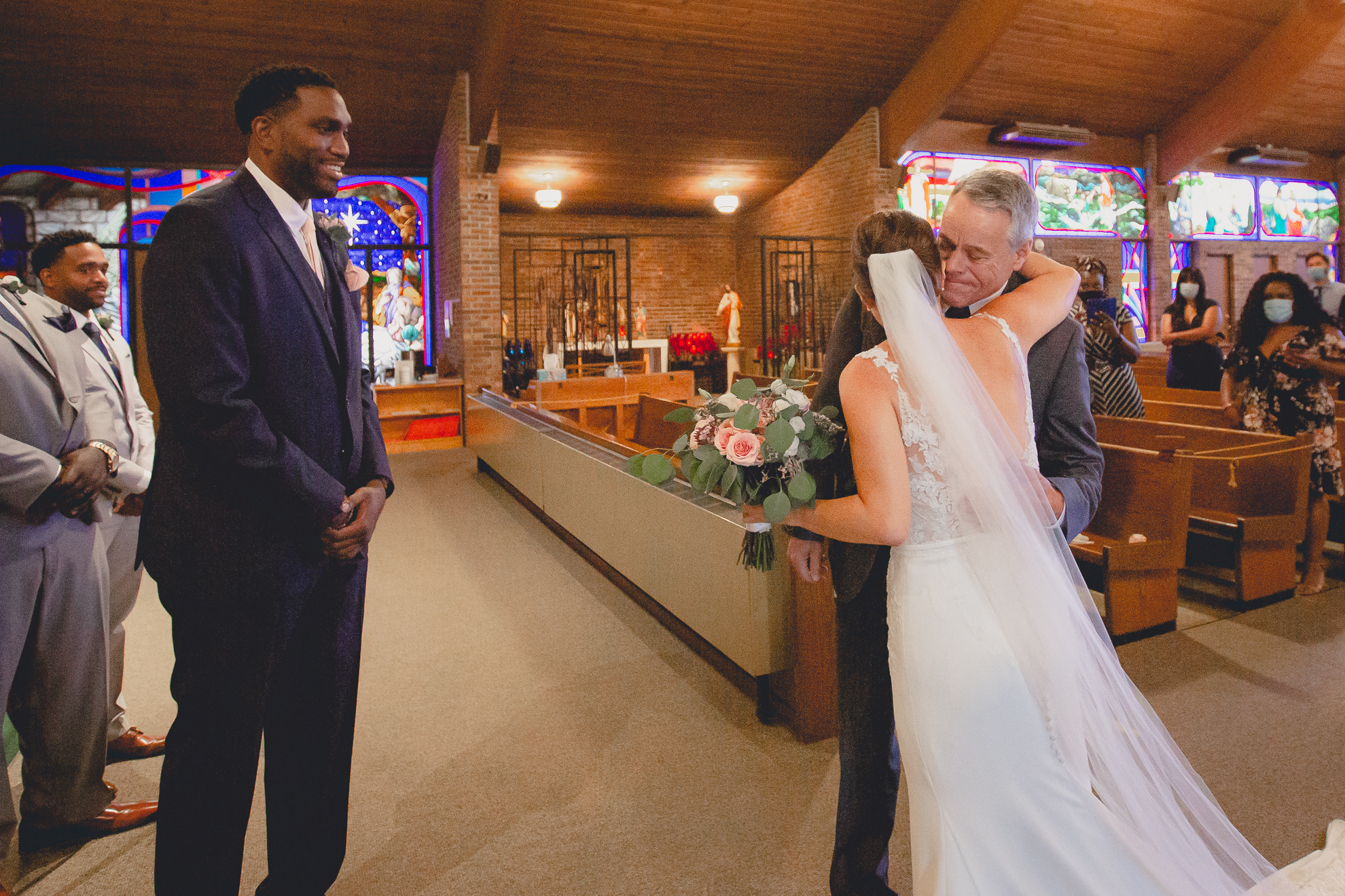 father hugs bride at end of aisle during micro wedding ceremony at St. Peter's Church in Lewiston, NY