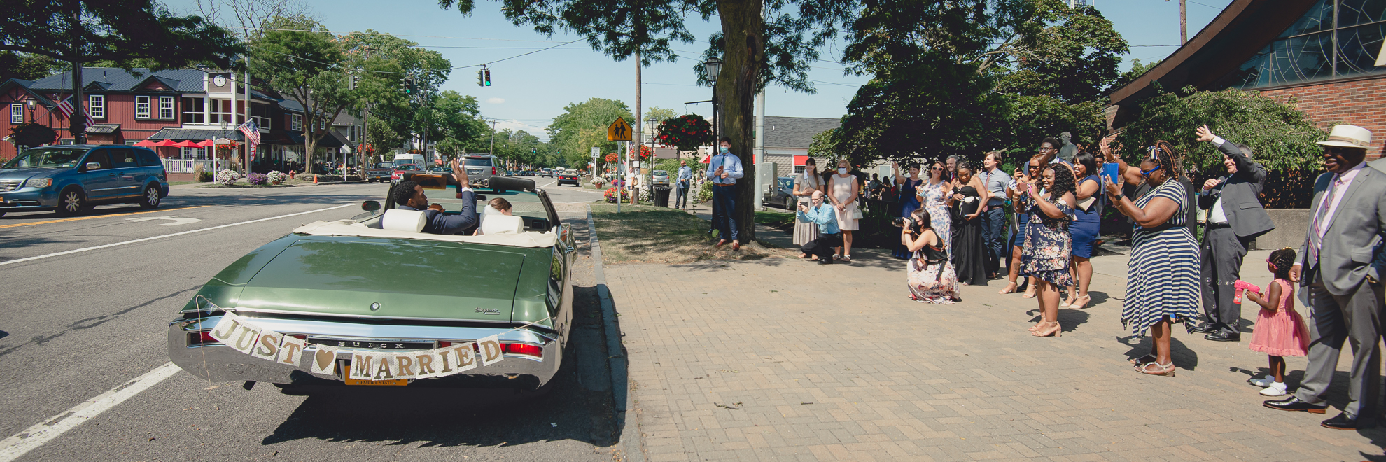 bride and groom wave to guests from vintage buick after micro wedding ceremony at St. Peter's Church in Lewiston, NY