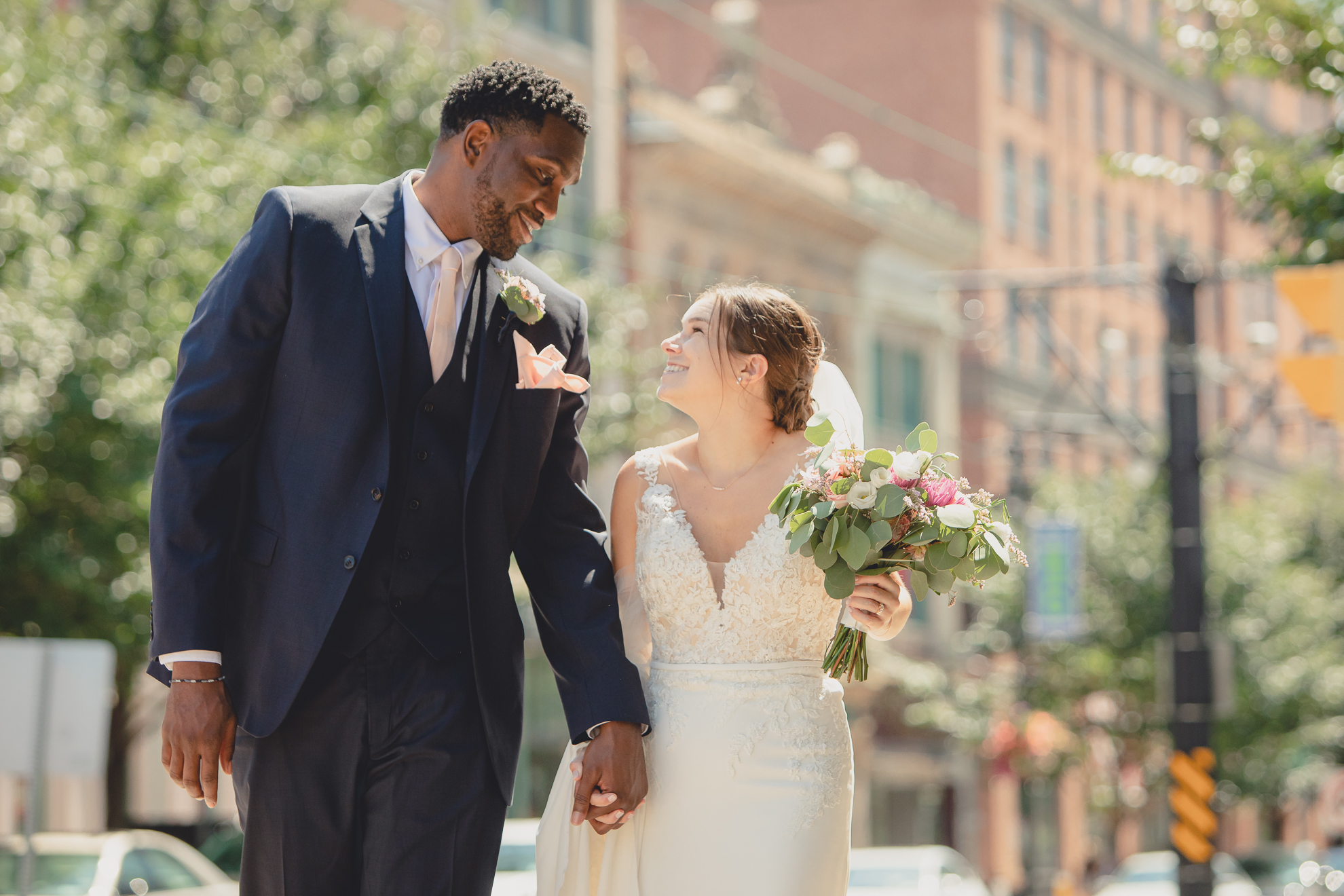 portraits of bride and groom smiling at each other while walking in theater district of Buffalo, NY near Shea's Theater during WNY micro wedding celebration