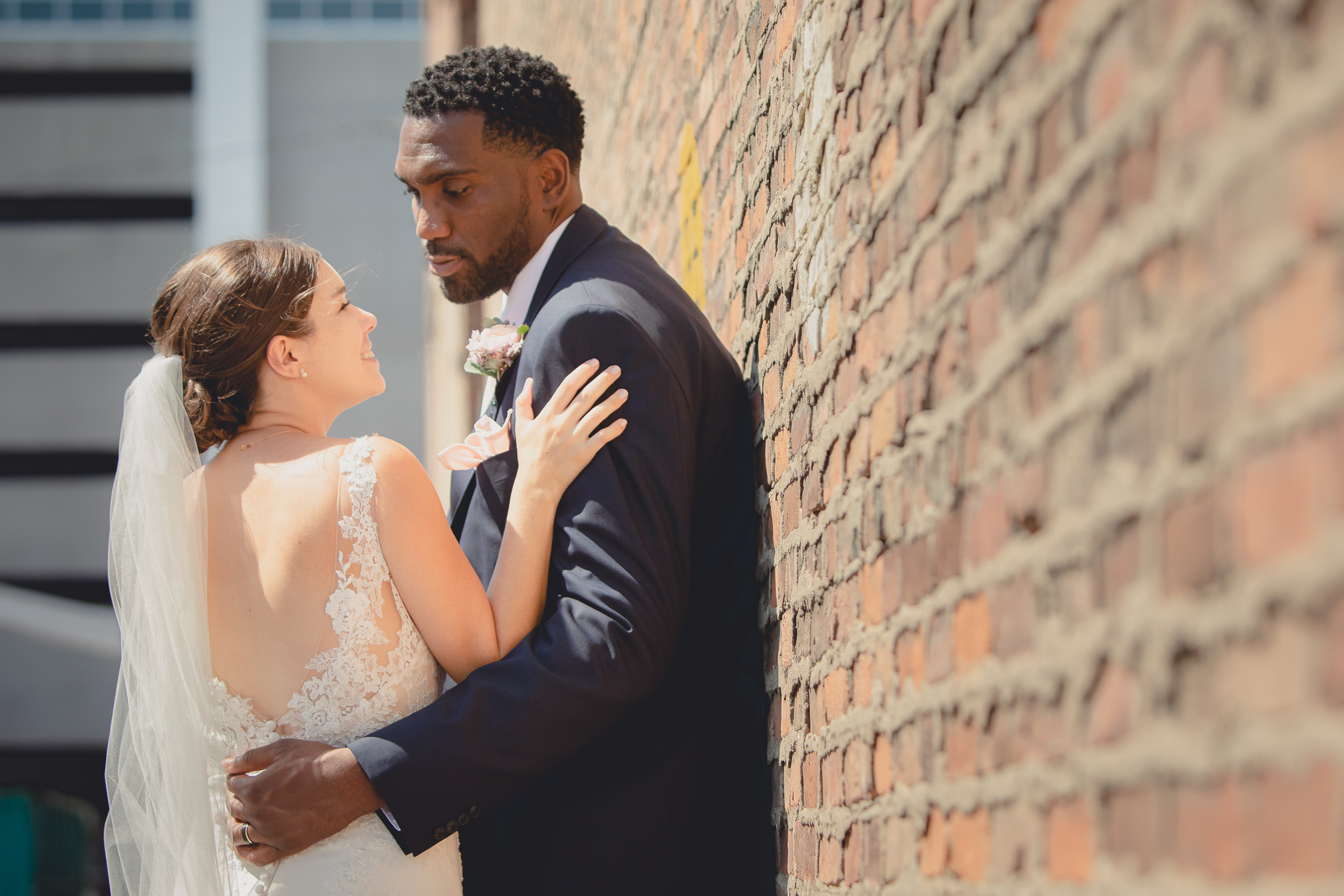 bride and groom look at each other along brick wall in theater district of Buffalo, NY near Shea's Theater during WNY micro wedding celebration