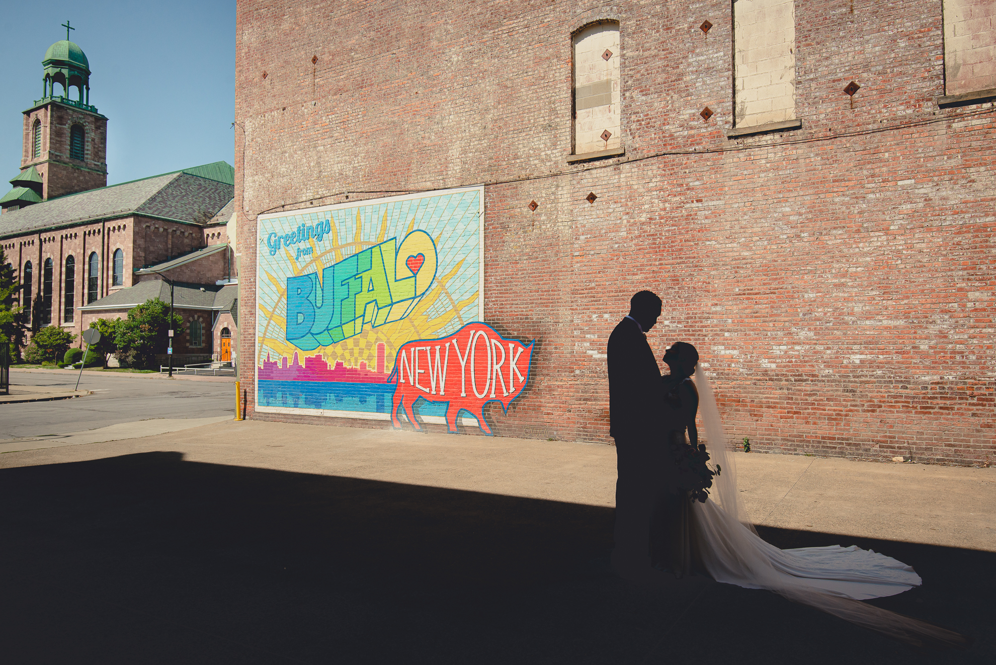 bride and groom look at each other in silhouette in theater district of Buffalo, NY at the "greetings from Buffalo" mural during WNY micro wedding celebration