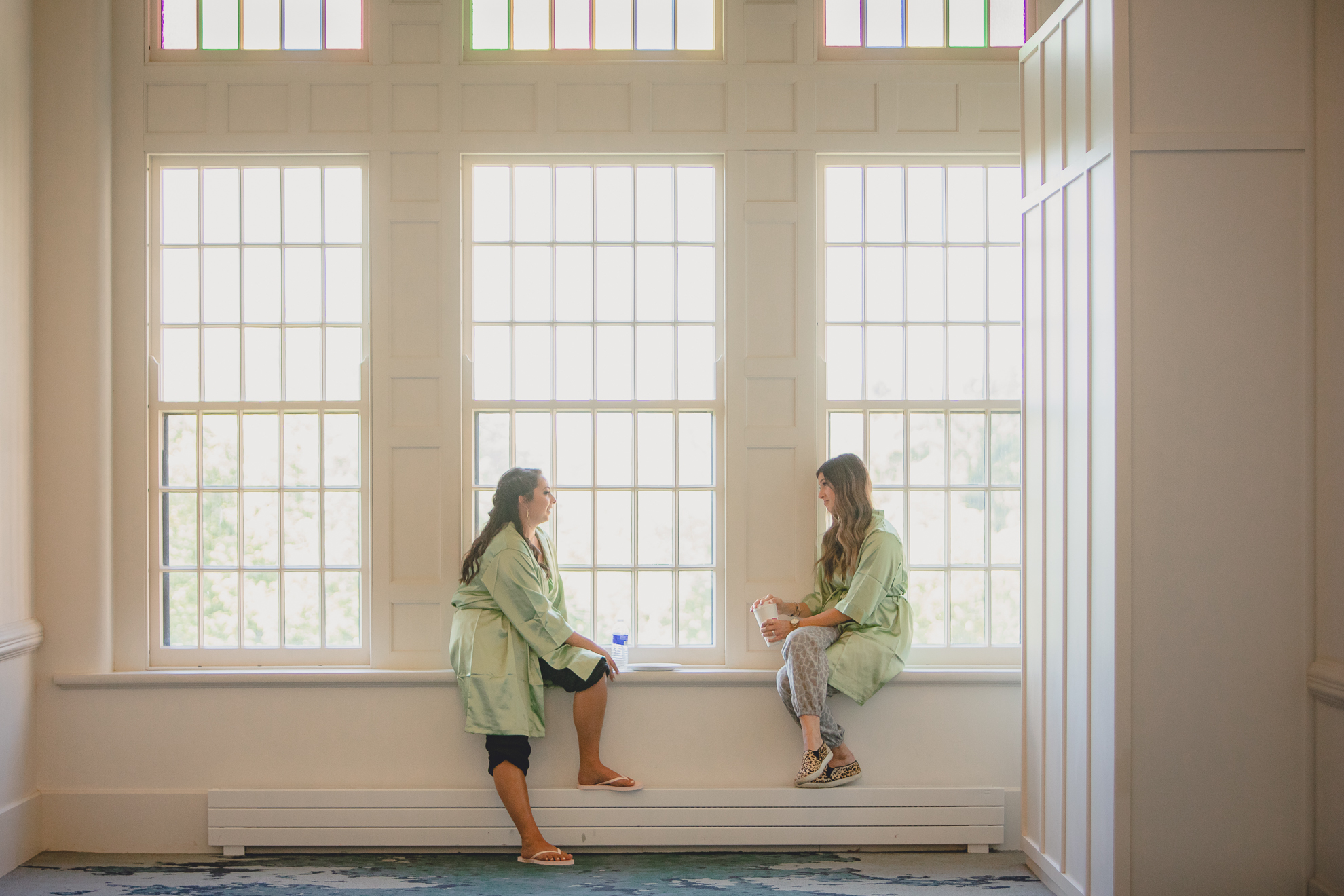 bridesmaids chat in large window before wedding at Hotel Henry in Buffalo, NY