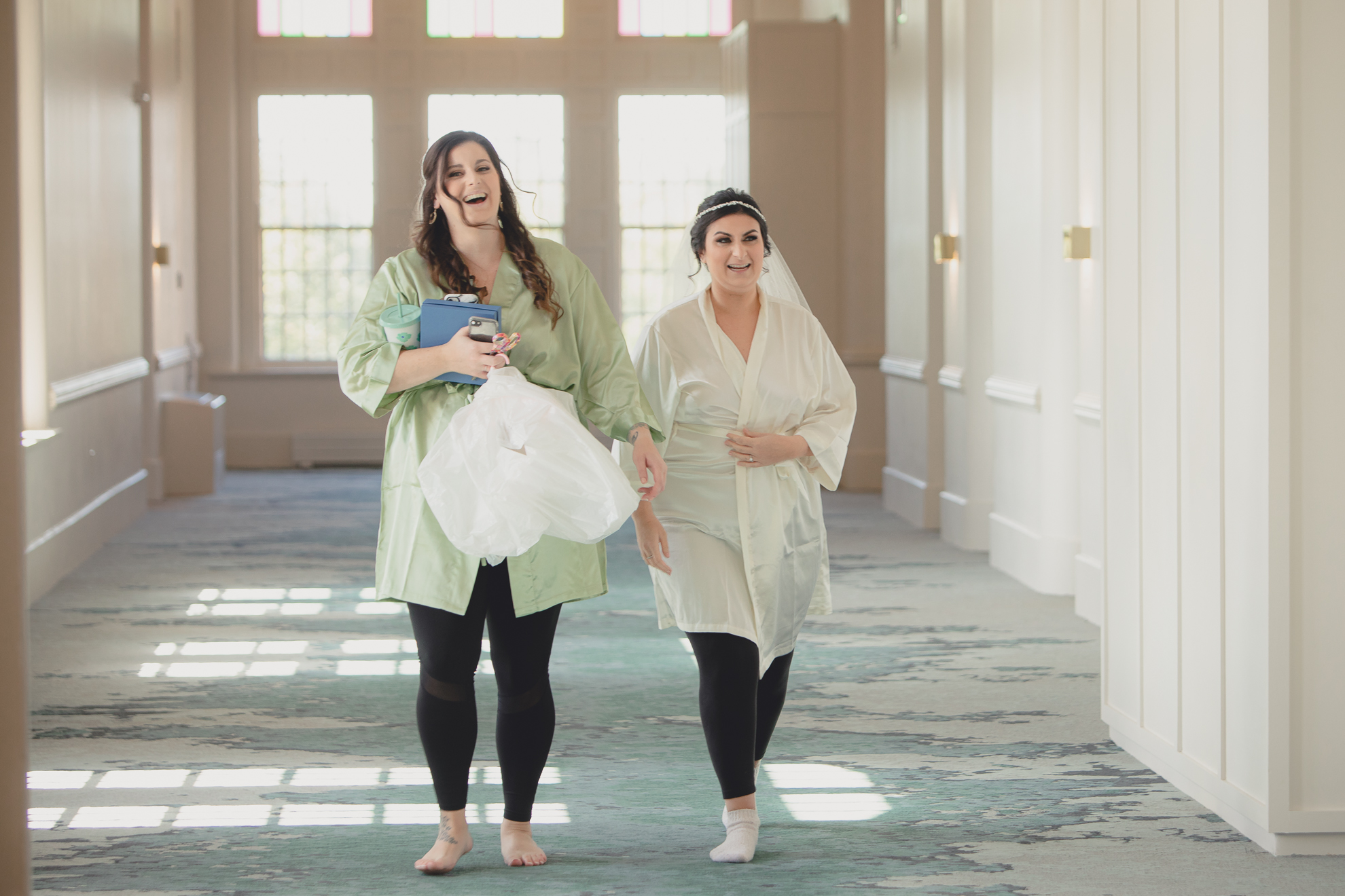 bride and bridesmaid laugh in hallway before wedding at Hotel Henry in Buffalo, NY