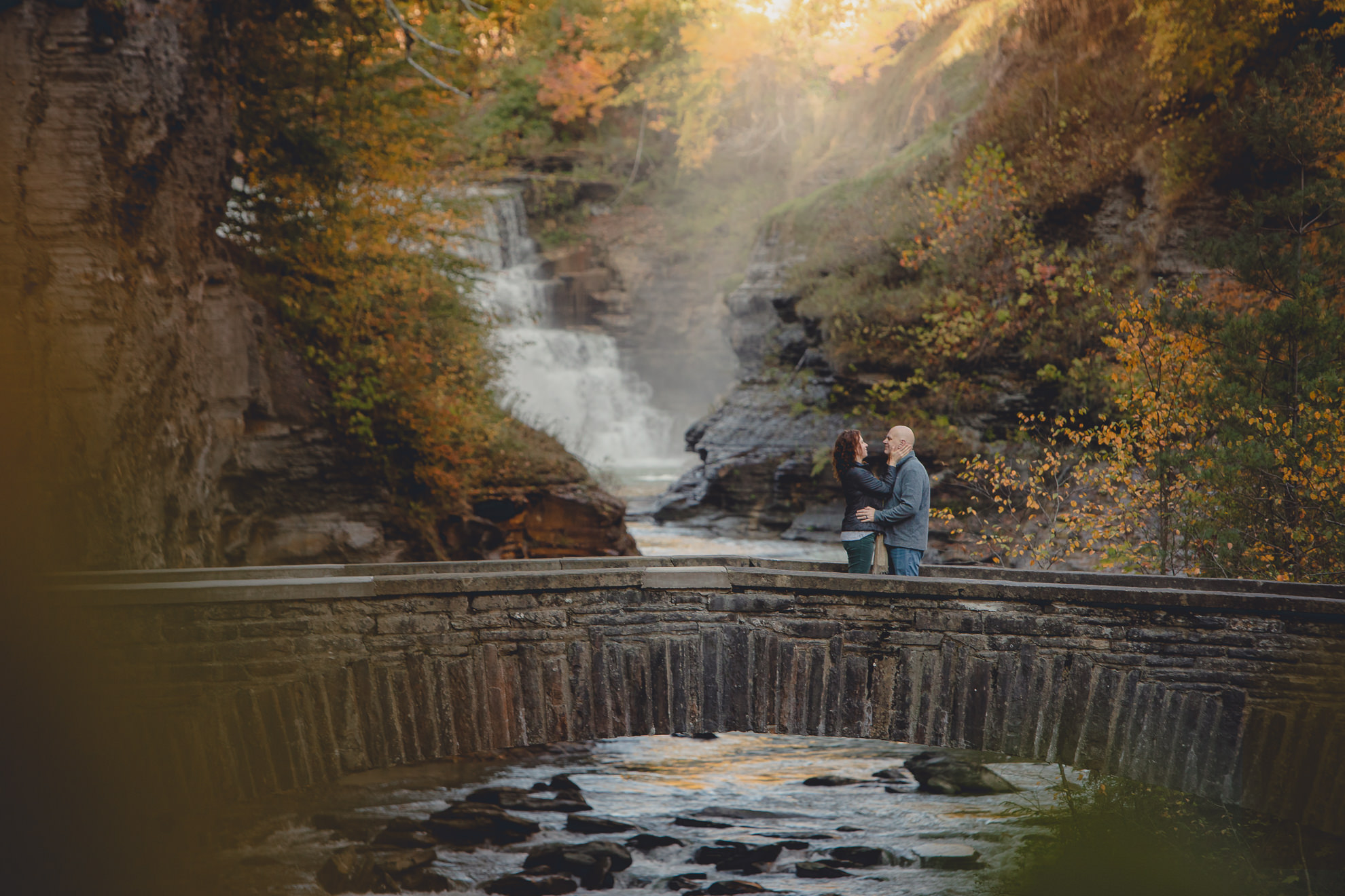 bride and groom embrace on bridge after wedding proposal in front of Falls at Letchworth State Park near Buffalo, NY
