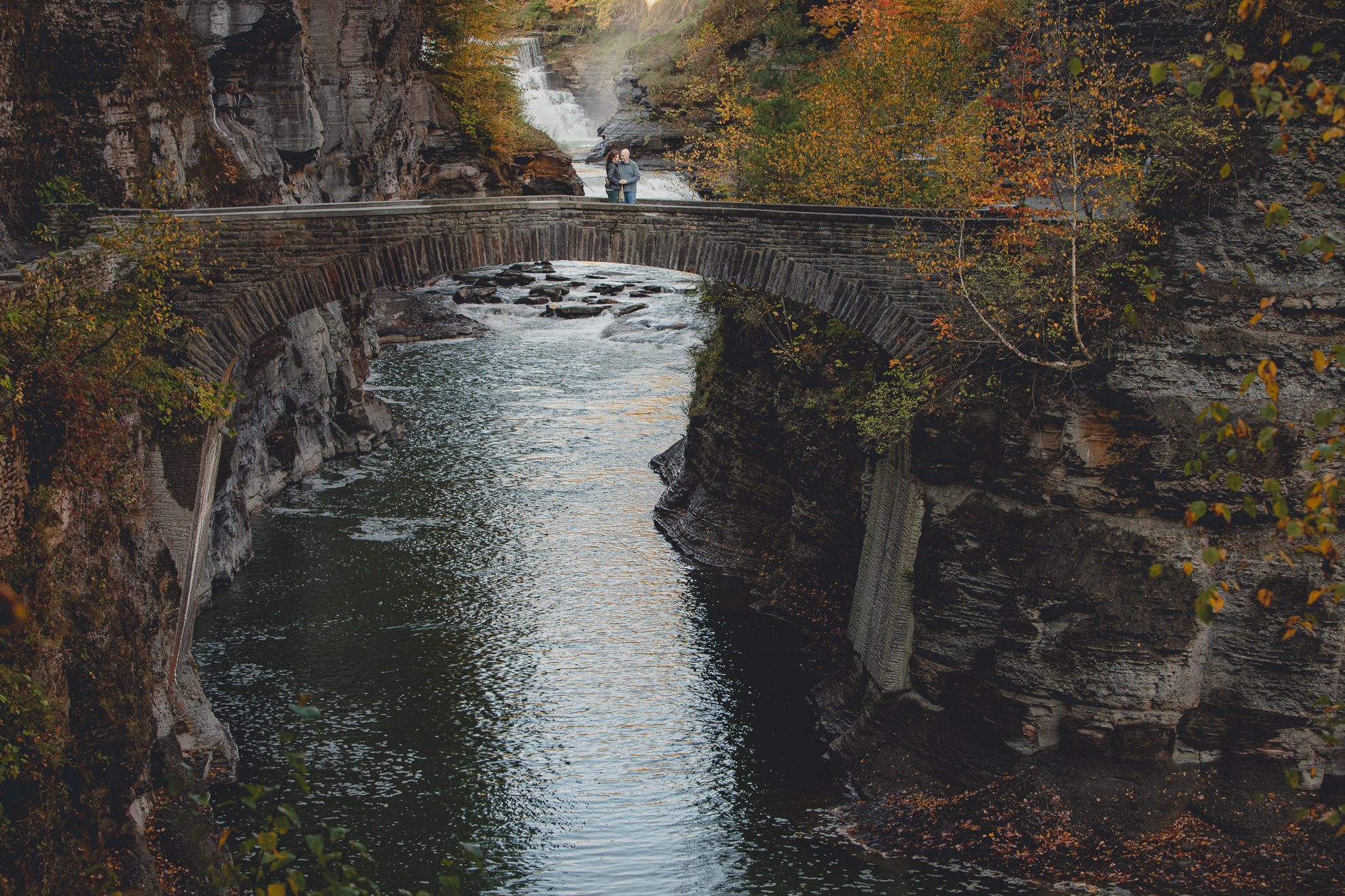 bride and groom embrace on bridge after wedding proposal in front of Falls at Letchworth State Park near Buffalo, NY