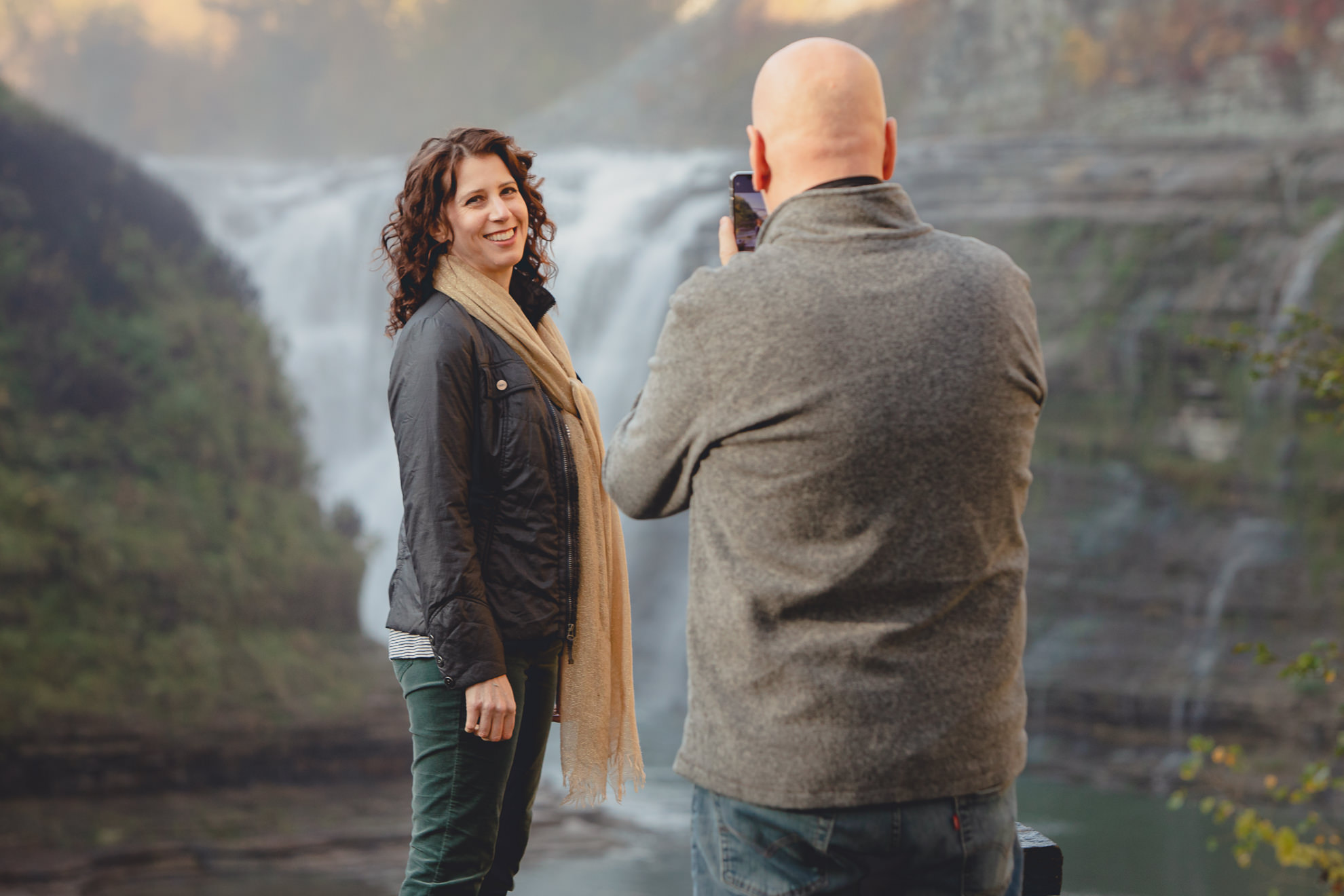 groom takes photo of bride in front of Upper Falls before wedding proposal at Letchworth State Park near Buffalo, NY