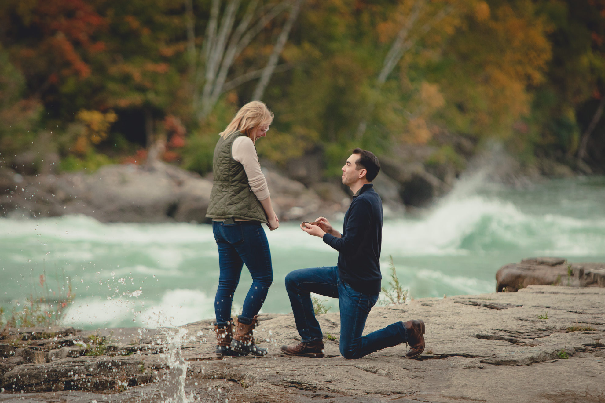 groom proposes marriage with rapids and fall foliage in background at Whirlpool State Park in Niagara Falls, NY