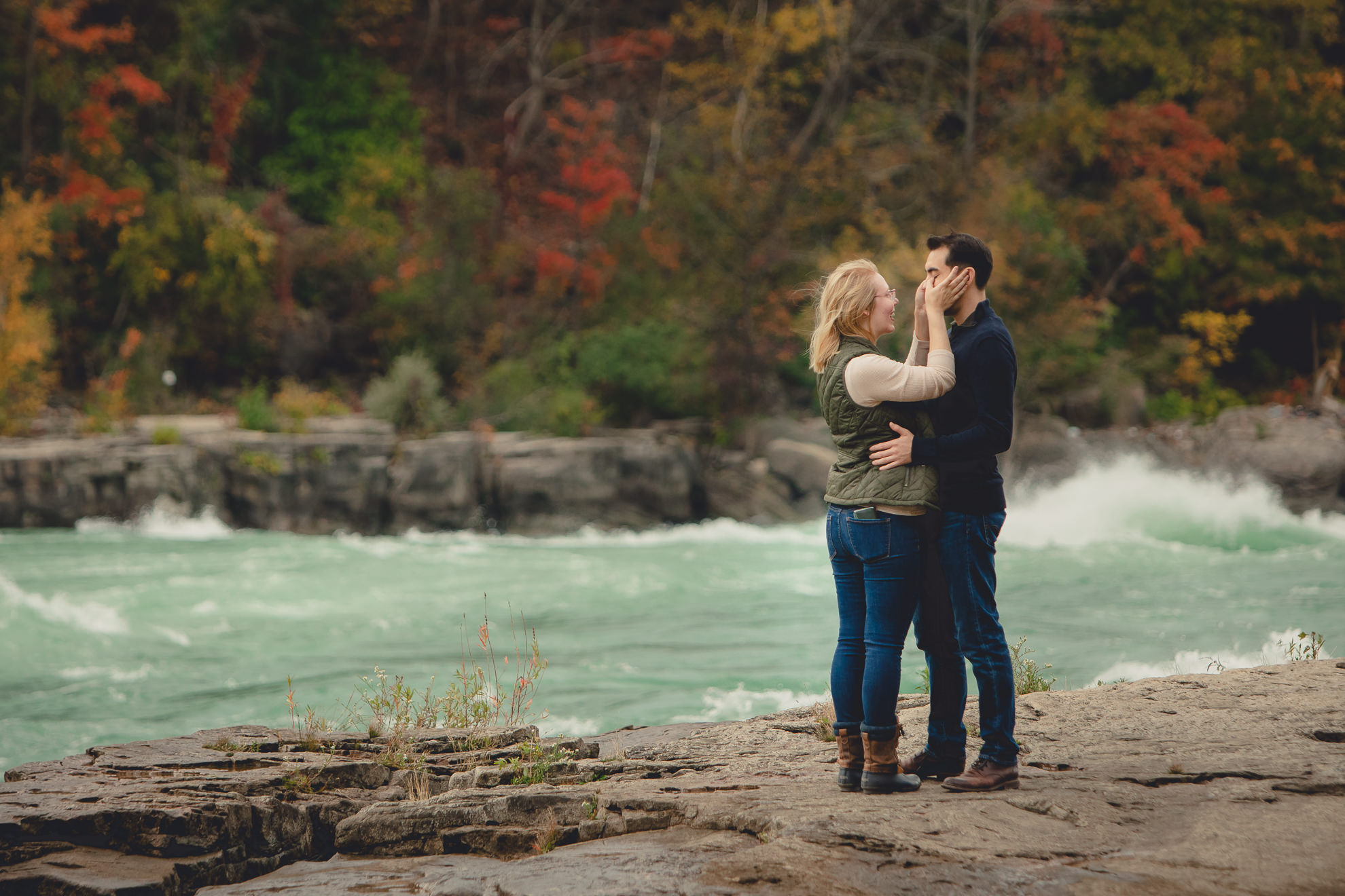 couple cries after wedding engagement proposal photography with rapids and fall foliage in background at Whirlpool State Park in Niagara Falls, NY
