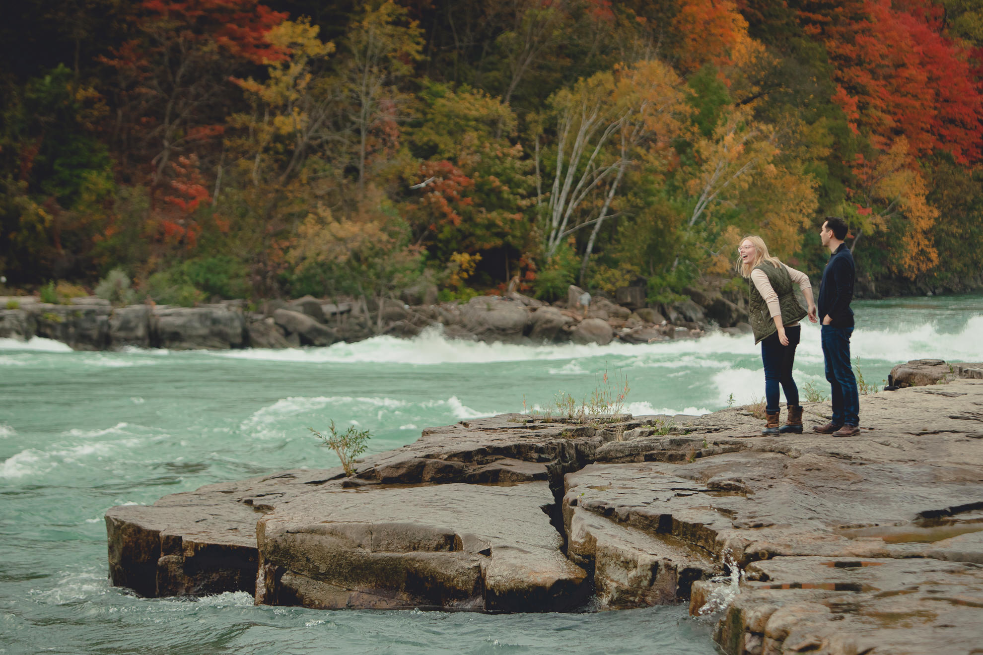 bride and groom admire rapids and fall foliage before wedding engagement proposal in Whirlpool State Park in Niagara Falls, NY