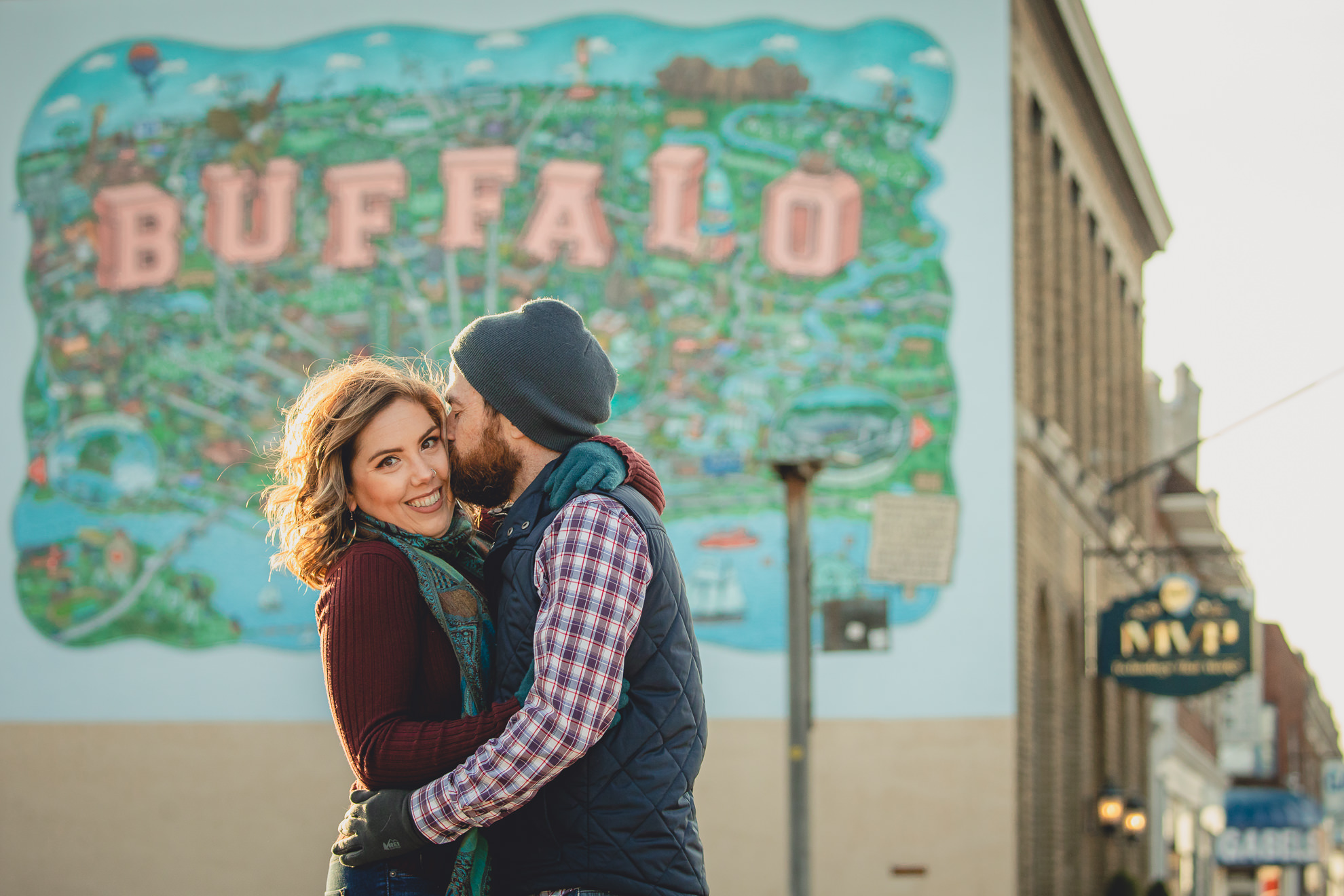 man kisses woman on cheek in front of Buffalo mural on Hertel Ave. in North Buffalo, NY