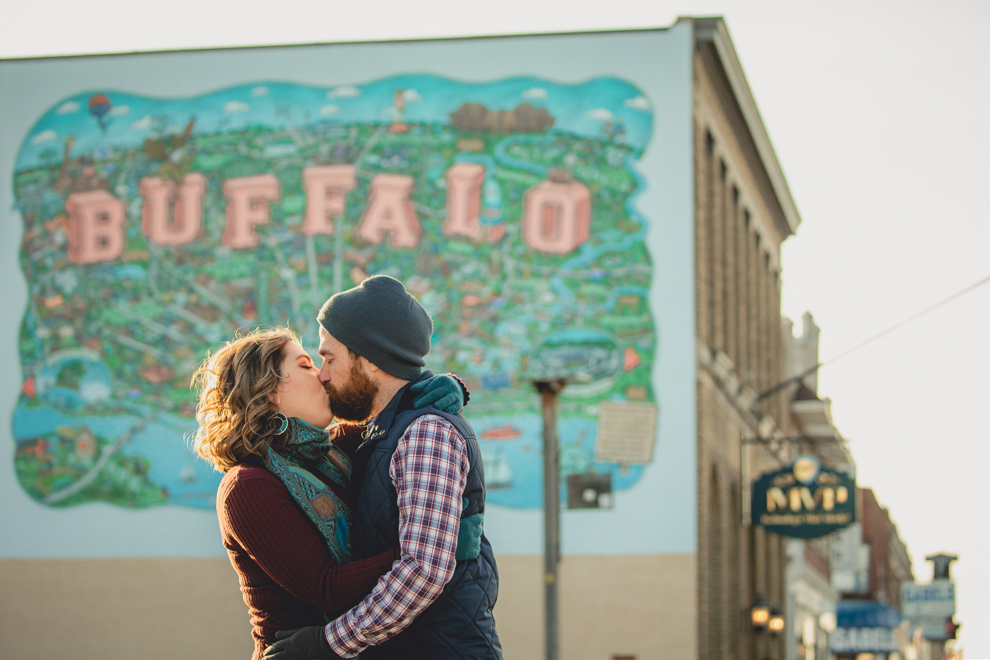 couple kisses while holding hands in front of Buffalo mural on Hertel Ave. in North Buffalo, NY during couples photography session