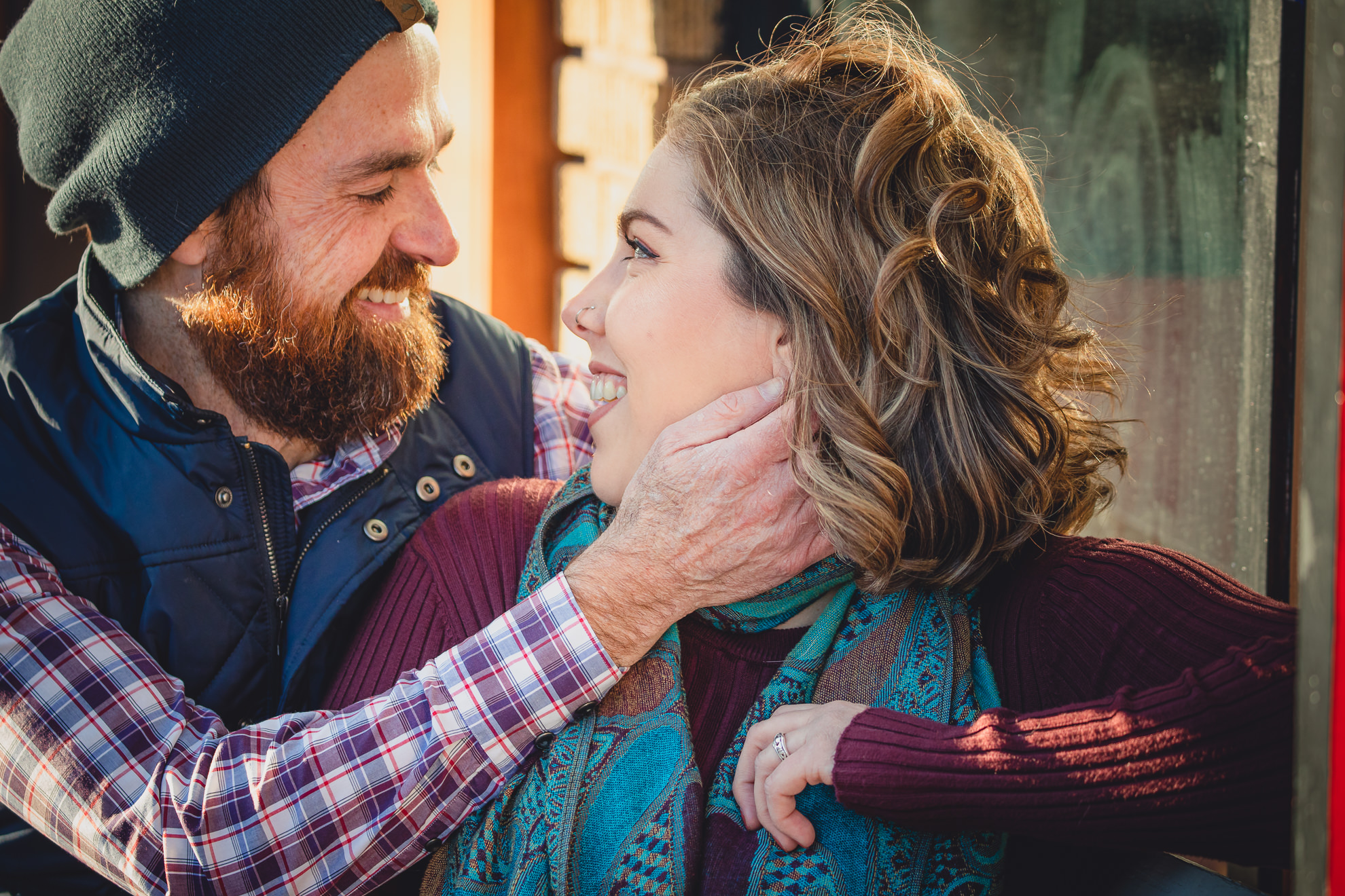 couple smiles at each other on bench in front of North Park Theater during couples mini photography session on Hertel Ave. in North Buffalo, NY