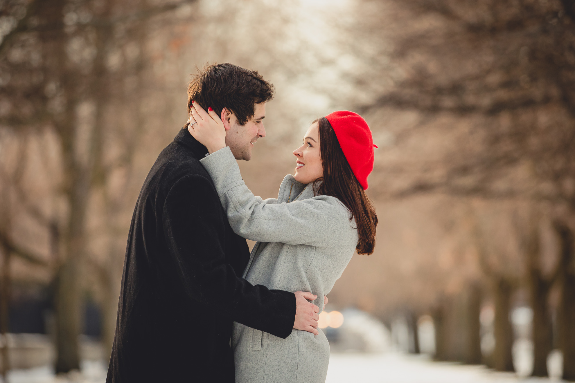 bride and groom look at one another smiling between the trees on Lincoln Parkway in Delaware Park during their wedding engagement photography session in Buffalo, NY