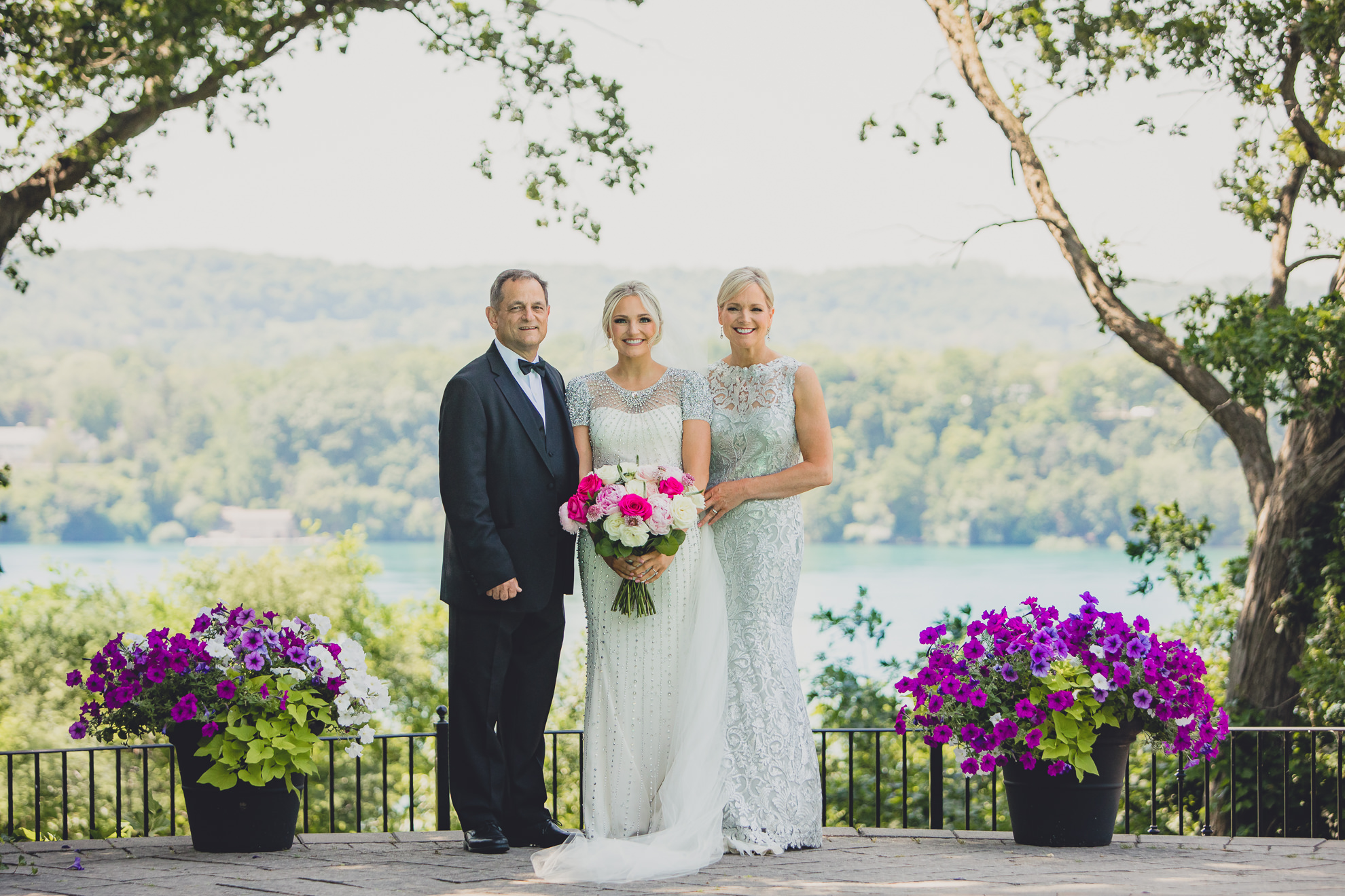 bride poses for portrait with parents in backyard along the Niagara River in Lewiston, NY