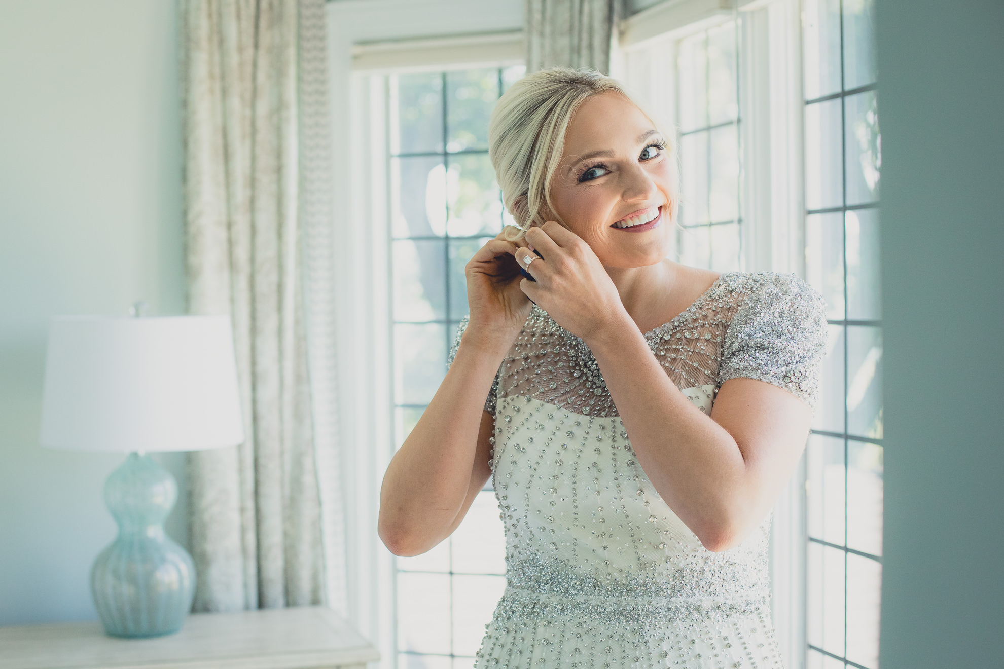 bride smiles while putting in earrings while getting ready for wedding in Lewiston, NY