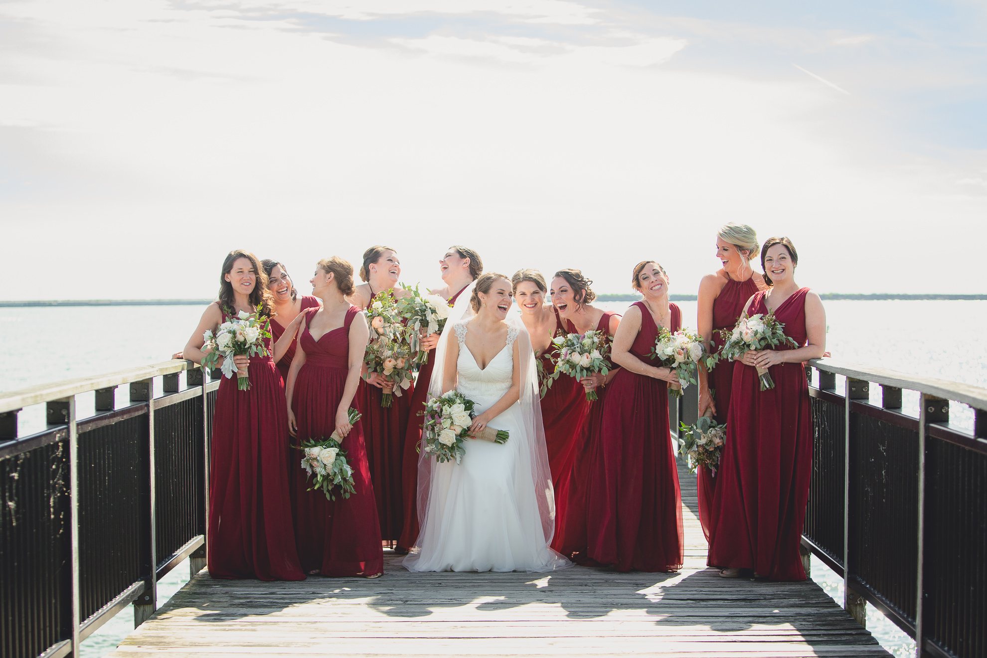 bride and bridesmaids pose for photographer at wedding on pier at Gallagher Beach on Outer Harbor of Buffalo, NY