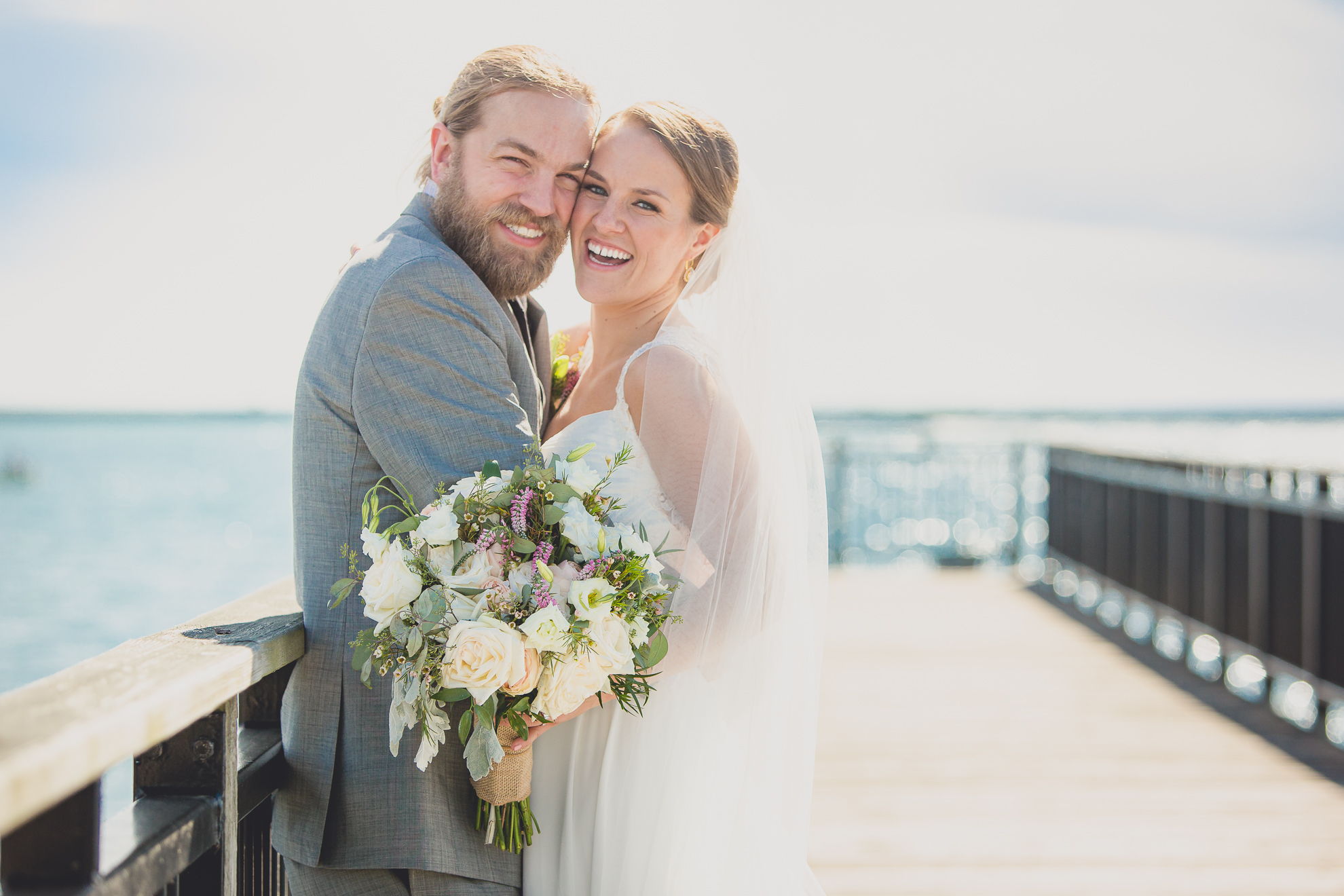 bride and groom pose for photographer at wedding on pier at Gallagher Beach on Outer Harbor of Buffalo, NY