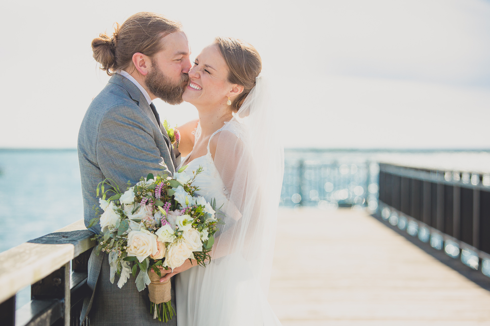 bride and groom pose for photographer at wedding on pier at Gallagher Beach on Outer Harbor of Buffalo, NY