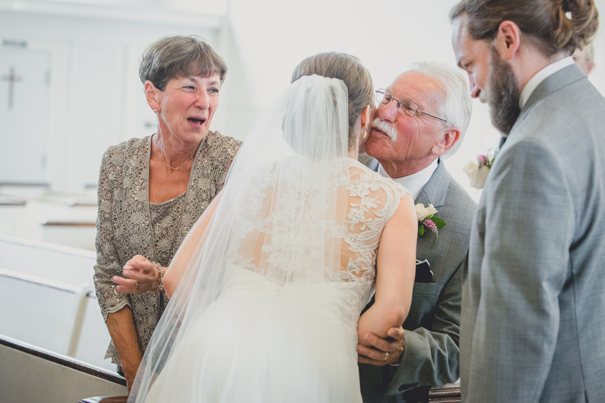 mother and father of groom hug bride during wedding ceremony at St. John the Baptist church in Kenmore, NY