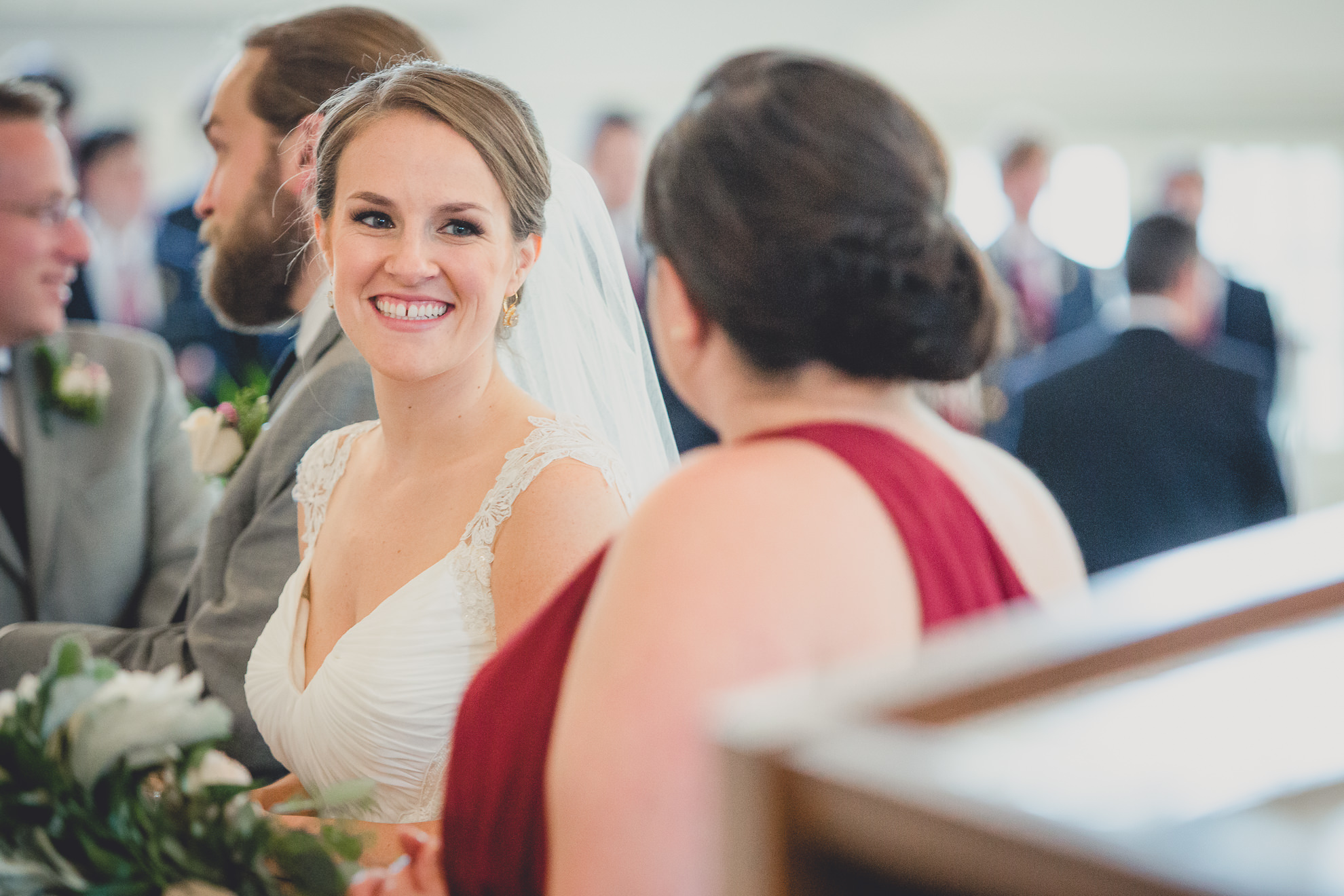 bride smiles at maid of honor during wedding ceremony at St. John the Baptist church in Kenmore, NY