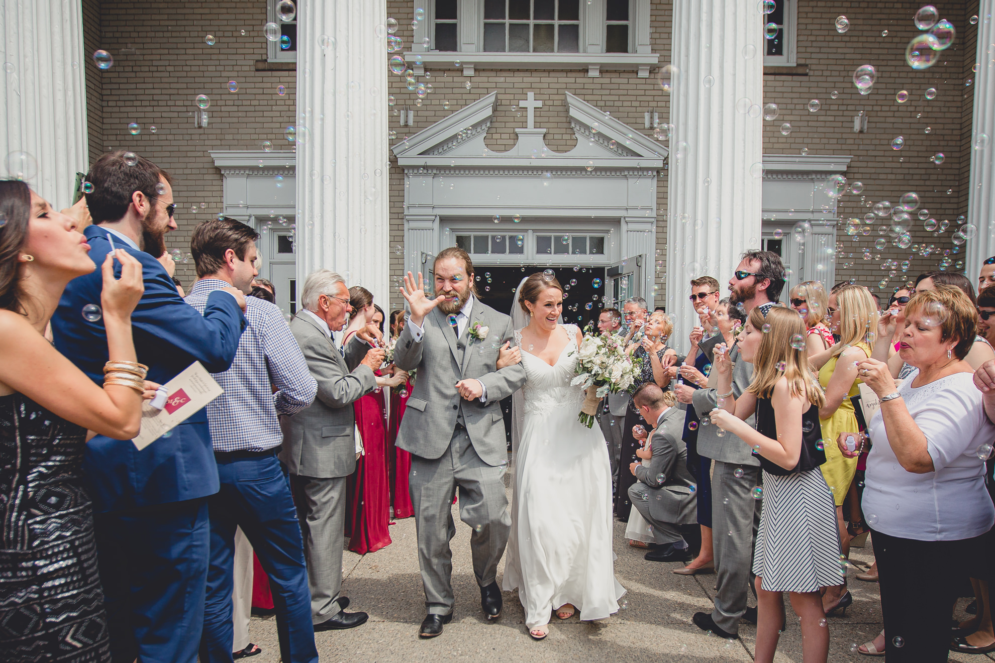 bride and groom exit church with bubbles after wedding ceremony at St. John the Baptist church in Kenmore, NY