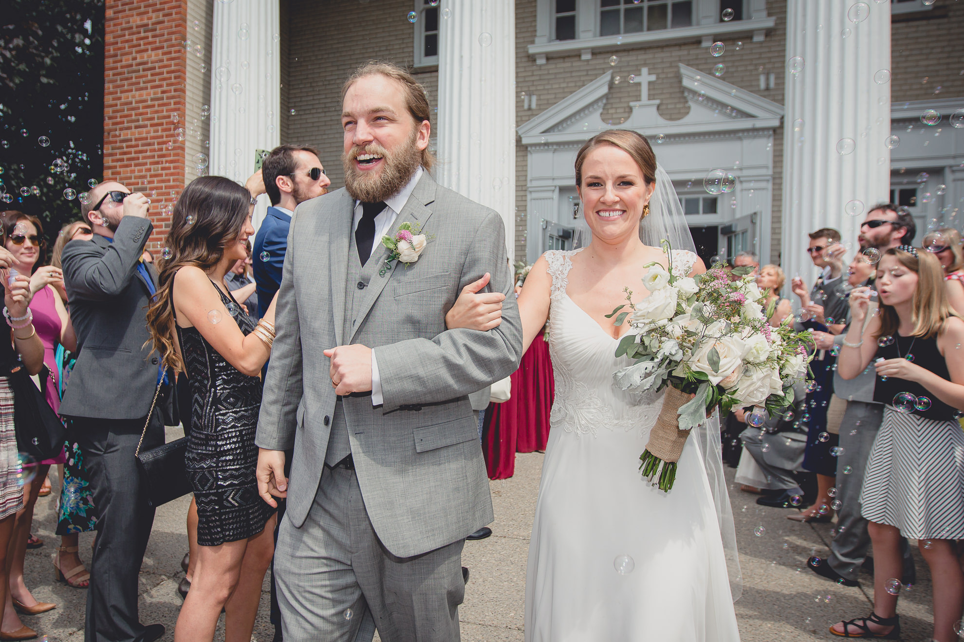 bride and groom exit church with bubbles after wedding ceremony at St. John the Baptist church in Kenmore, NY