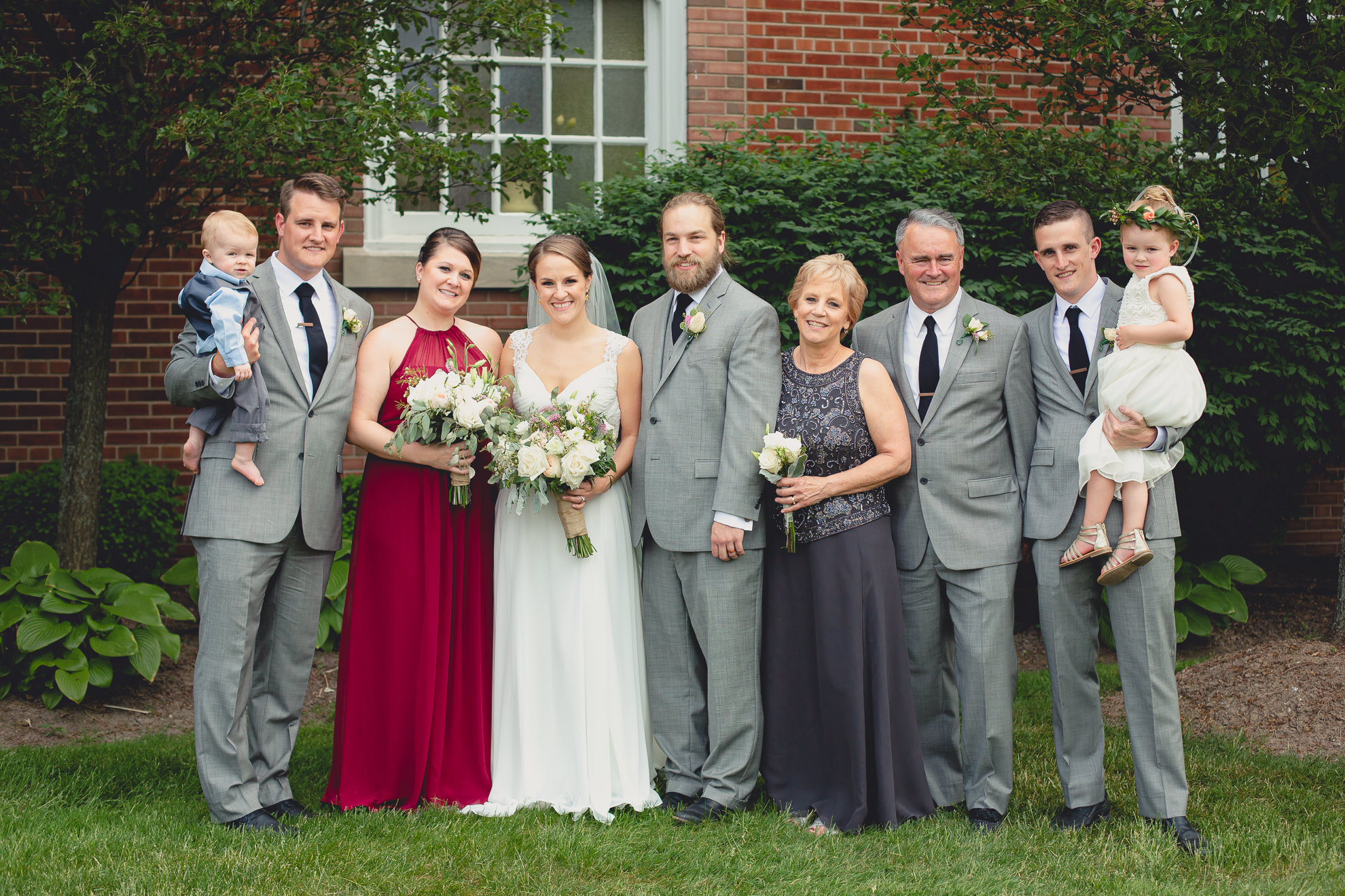 bride, groom and family pose for portrait with photographer at St. John the Baptist church in Kenmore, NY