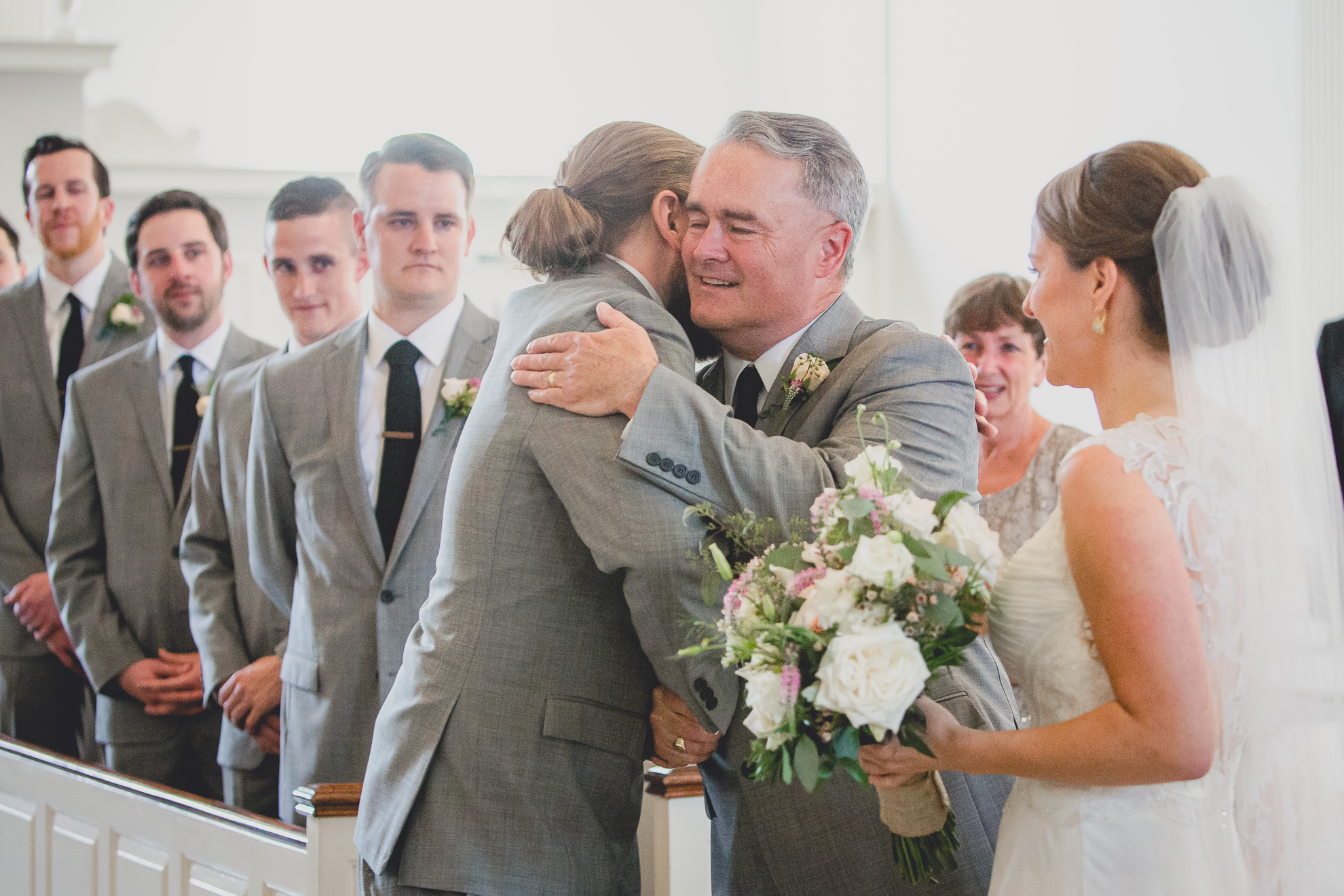 groom hugs father of bride during wedding ceremony at St. John the Baptist church in Kenmore, NY