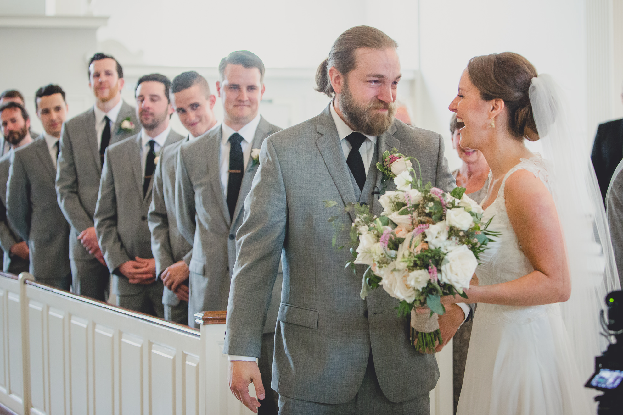 groom cries while looking at bride during processional during wedding ceremony at St. John the Baptist church in Kenmore, NY