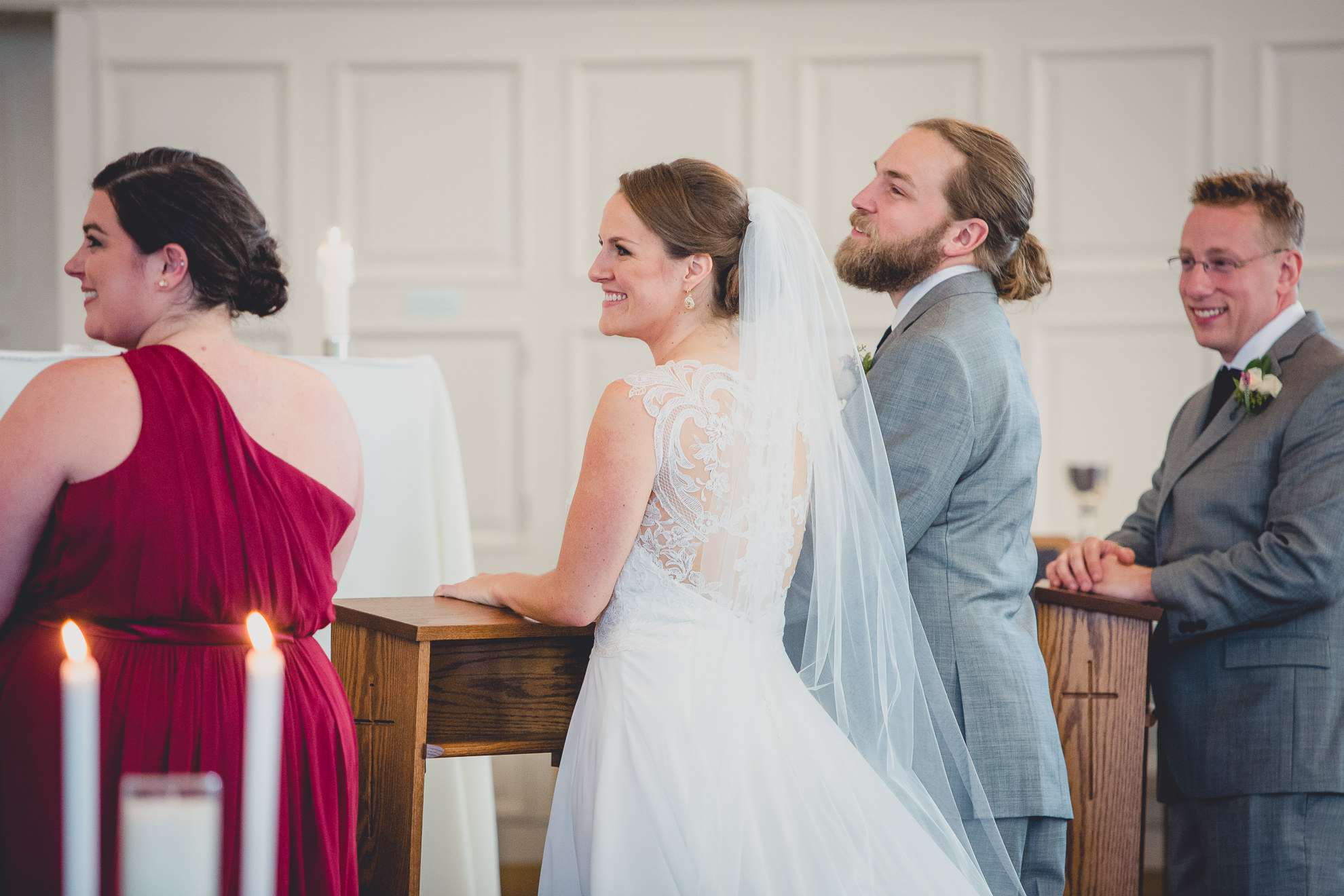 bride and groom smile at priest during wedding ceremony at St. John the Baptist church in Kenmore, NY