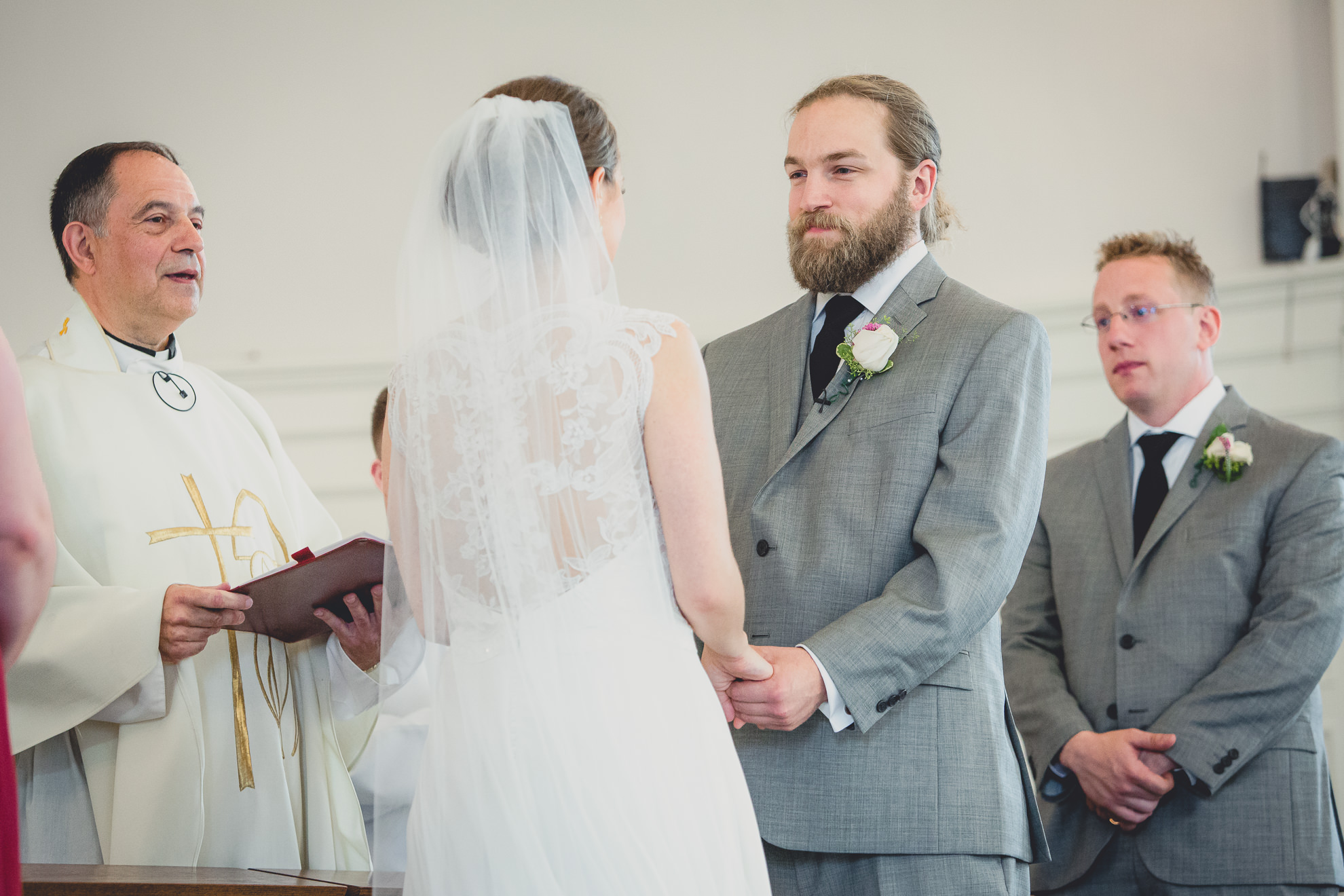 groom looks at bride during vows during wedding ceremony at St. John the Baptist church in Kenmore, NY